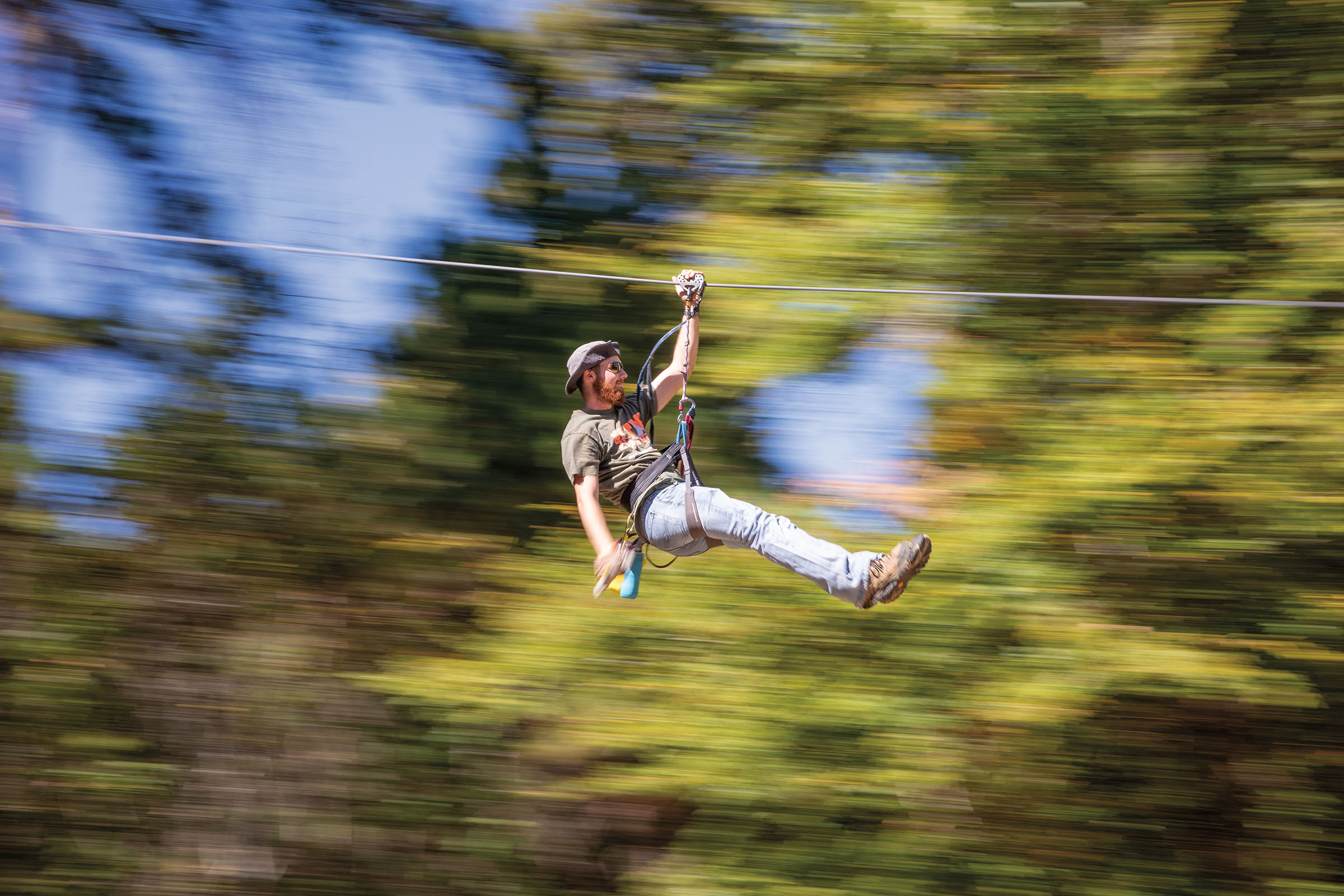 A person wearing long pants and a helmet whizzes through the air in front of green trees
