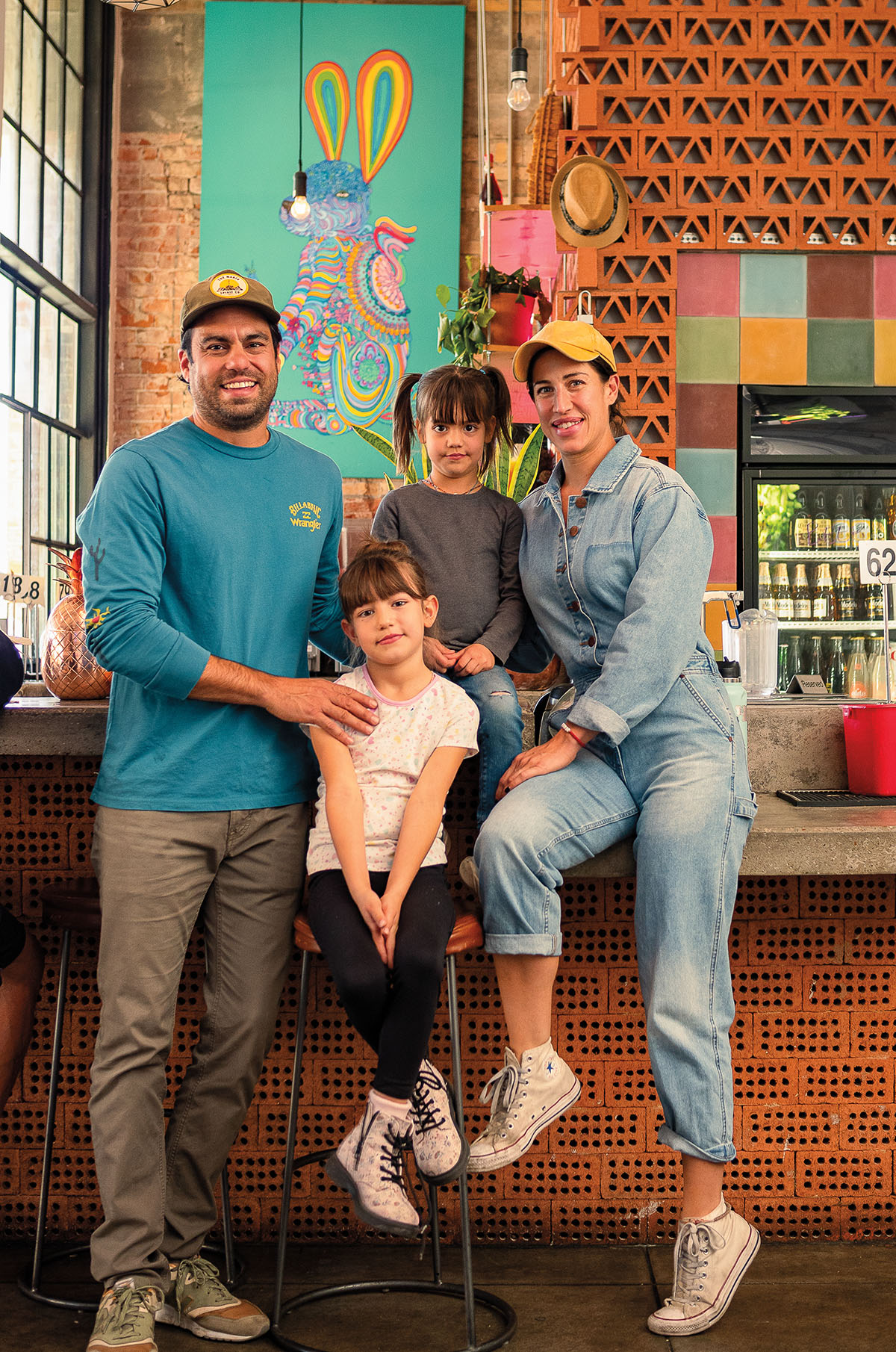 A group of people smile while sitting on the counter of a brightly-colored restaurant