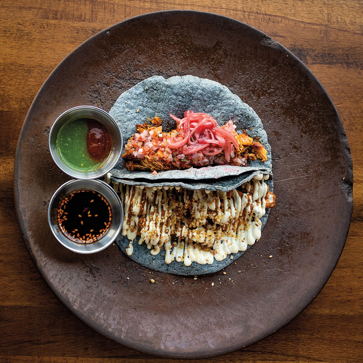 An overhead view of blue corn tacos on a dark plate