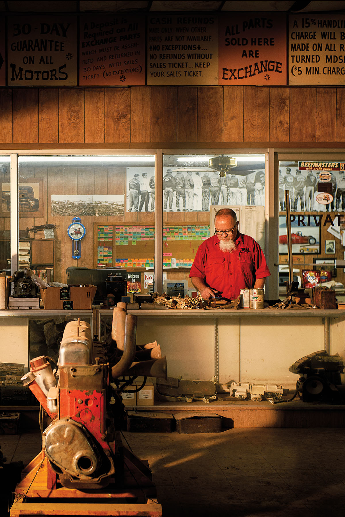 A man wearing a bright red shirt stands at a counter on a cell phone