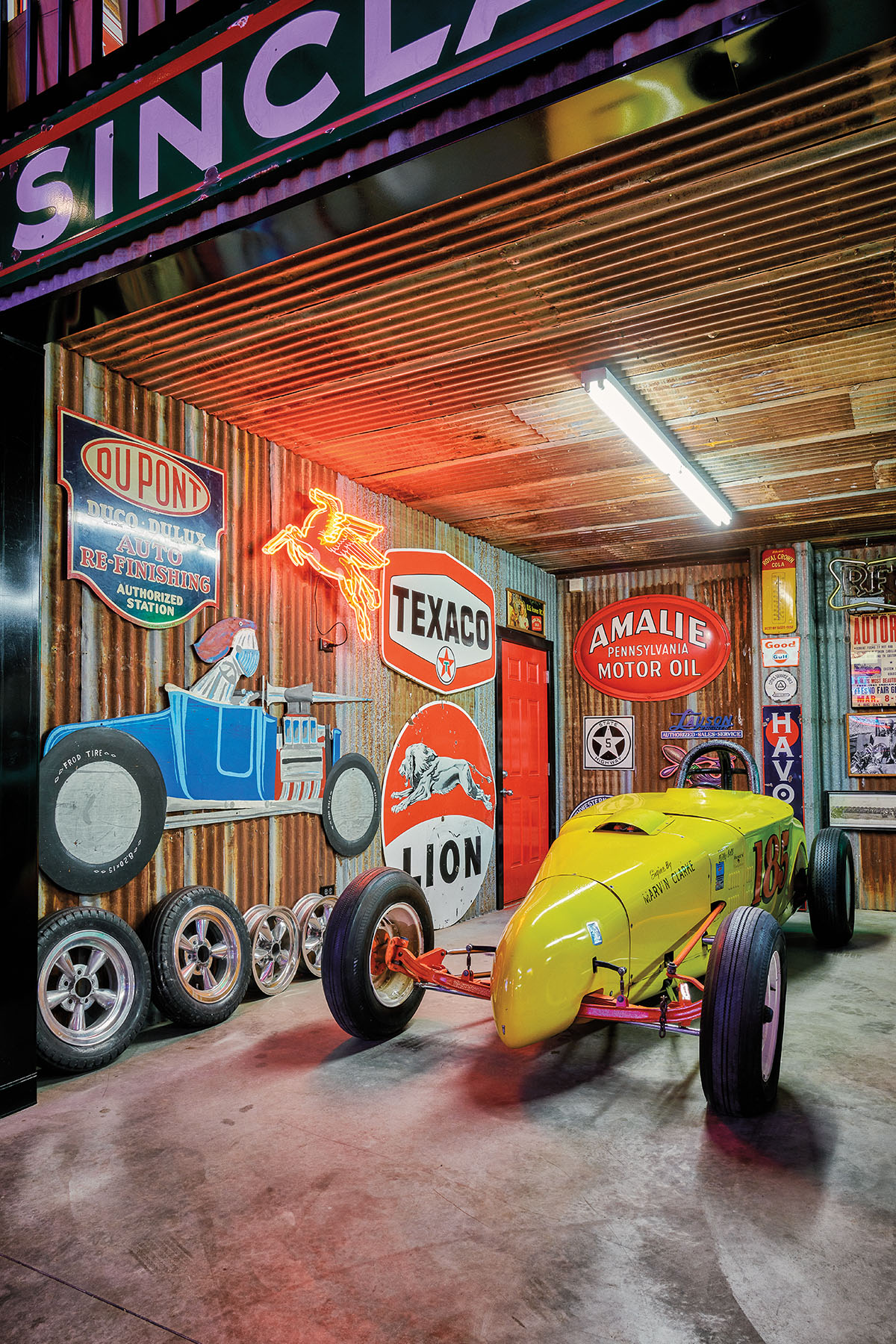 A bright yellow dragster car in a harshly-lit showroom with numerous wall decorations