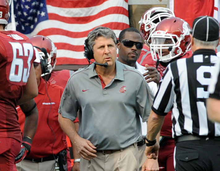Coach Mike Leach wearing a Washington State University jersey and a headset in front of an American flag