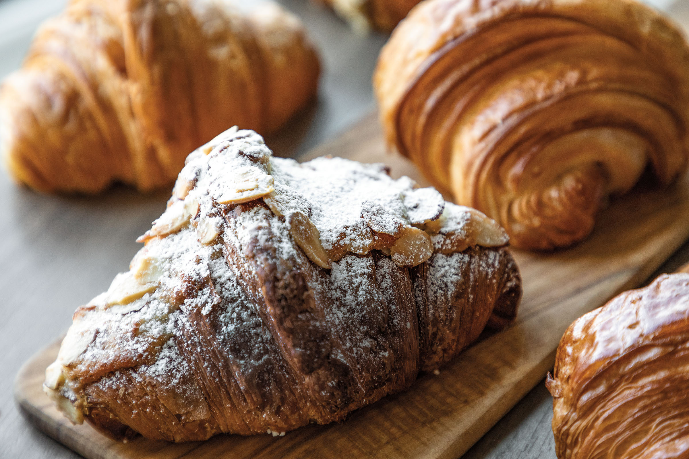 Golden croissants, one topped with powdered sugar and sliced almonds