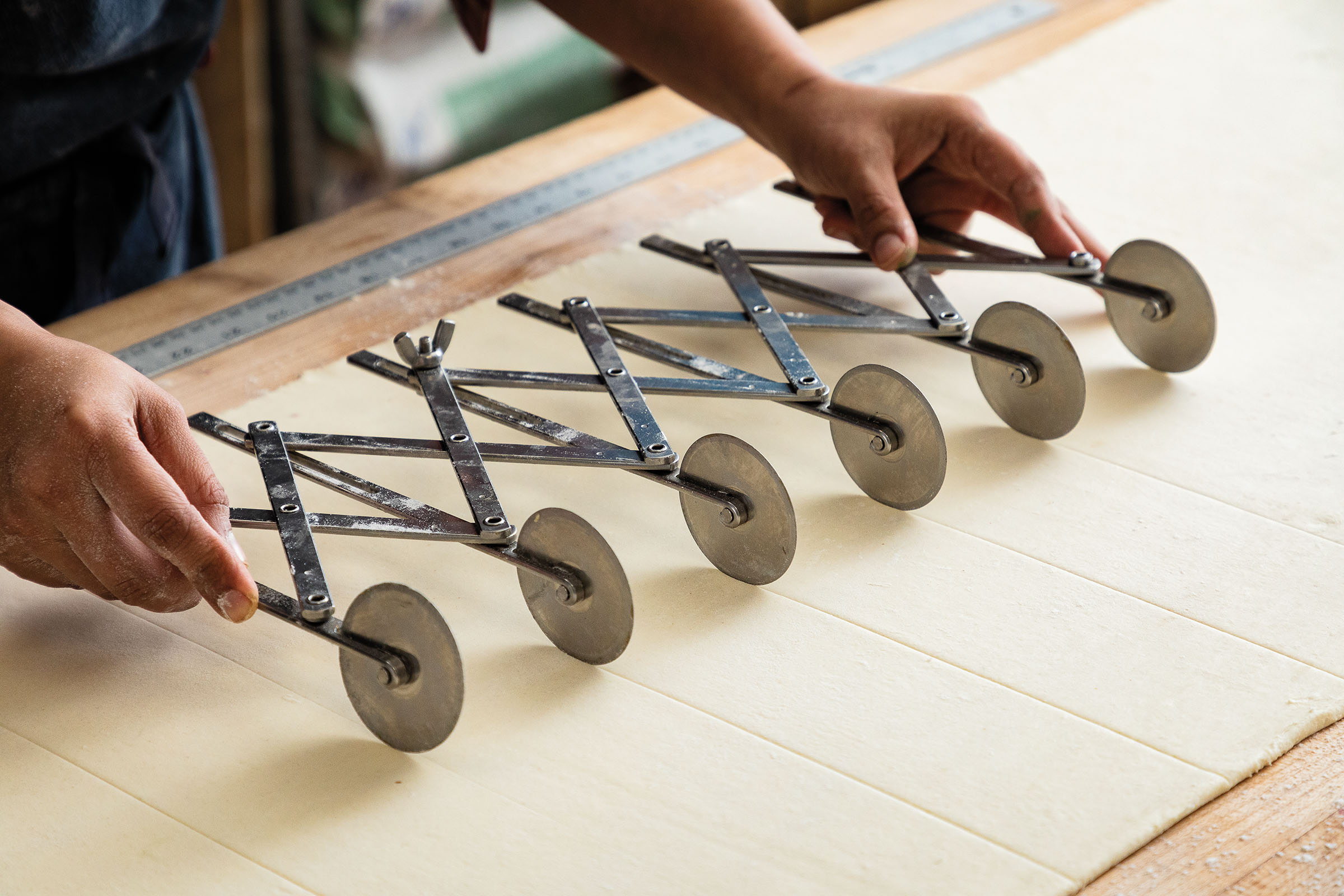 Silver wheels attached to a large handle move across dough leaving precision straight lines