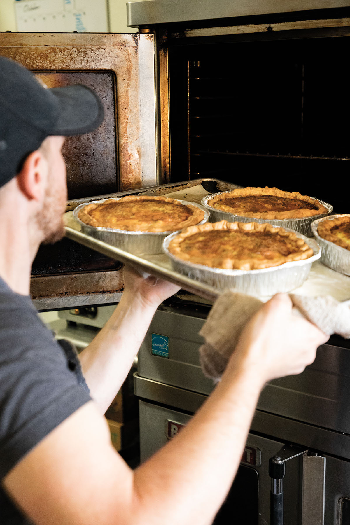 A man carefully loads pies into a warming drawer on a silver baking sheet