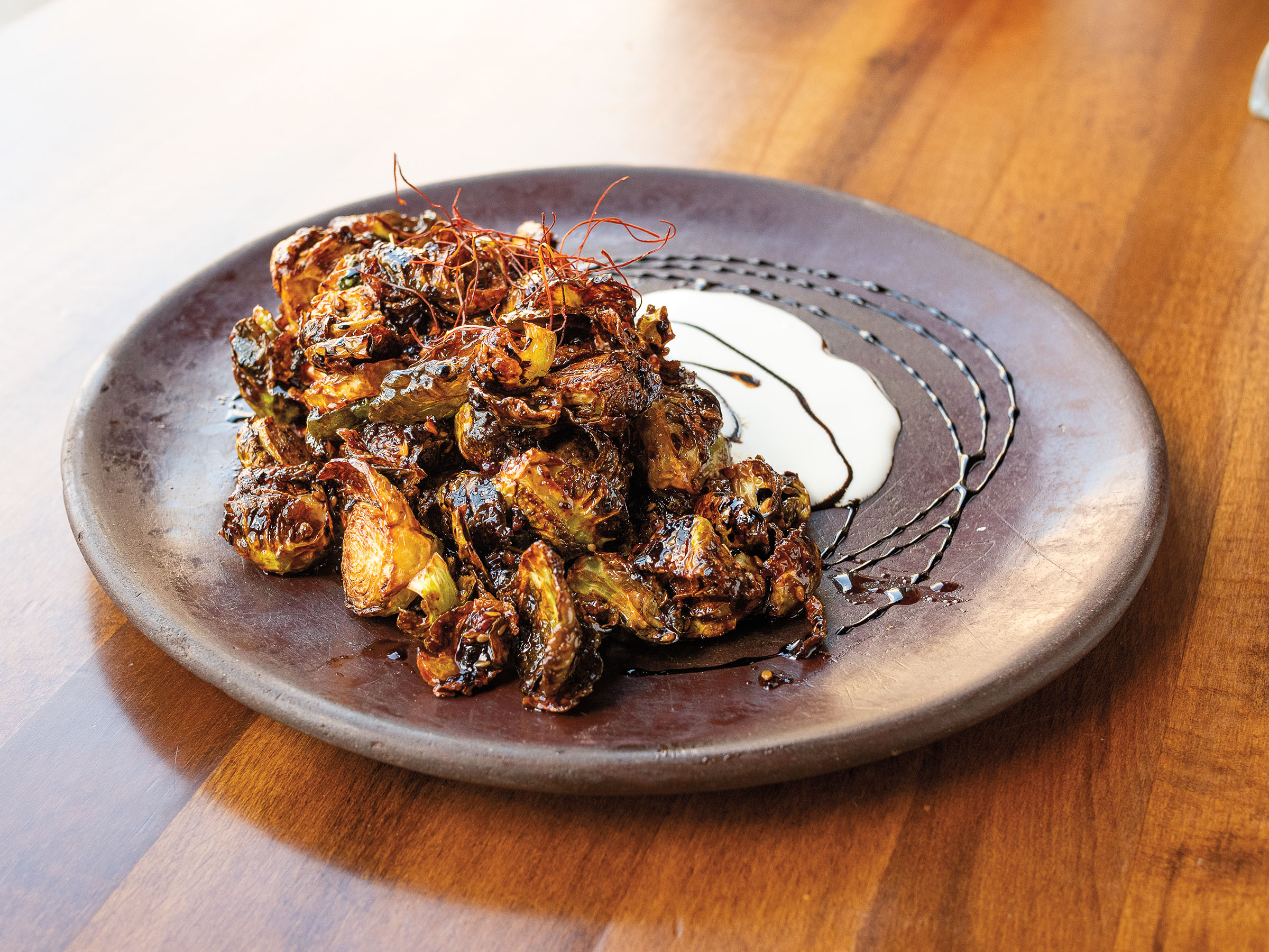 A pile of brussels sprouts with crema on a dark plate