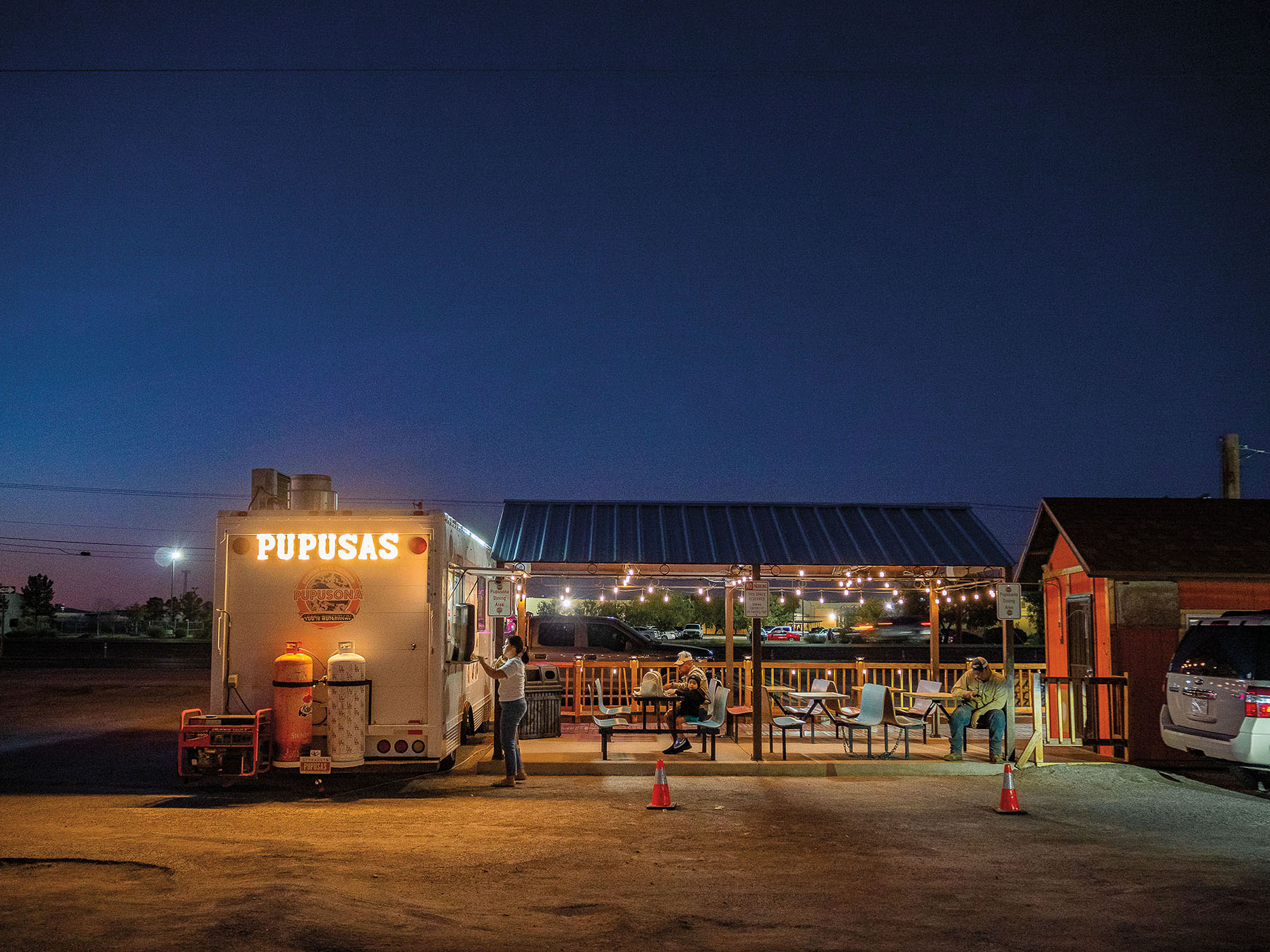 The exterior of a taco truck with a glowing sign reading "Pupusas"