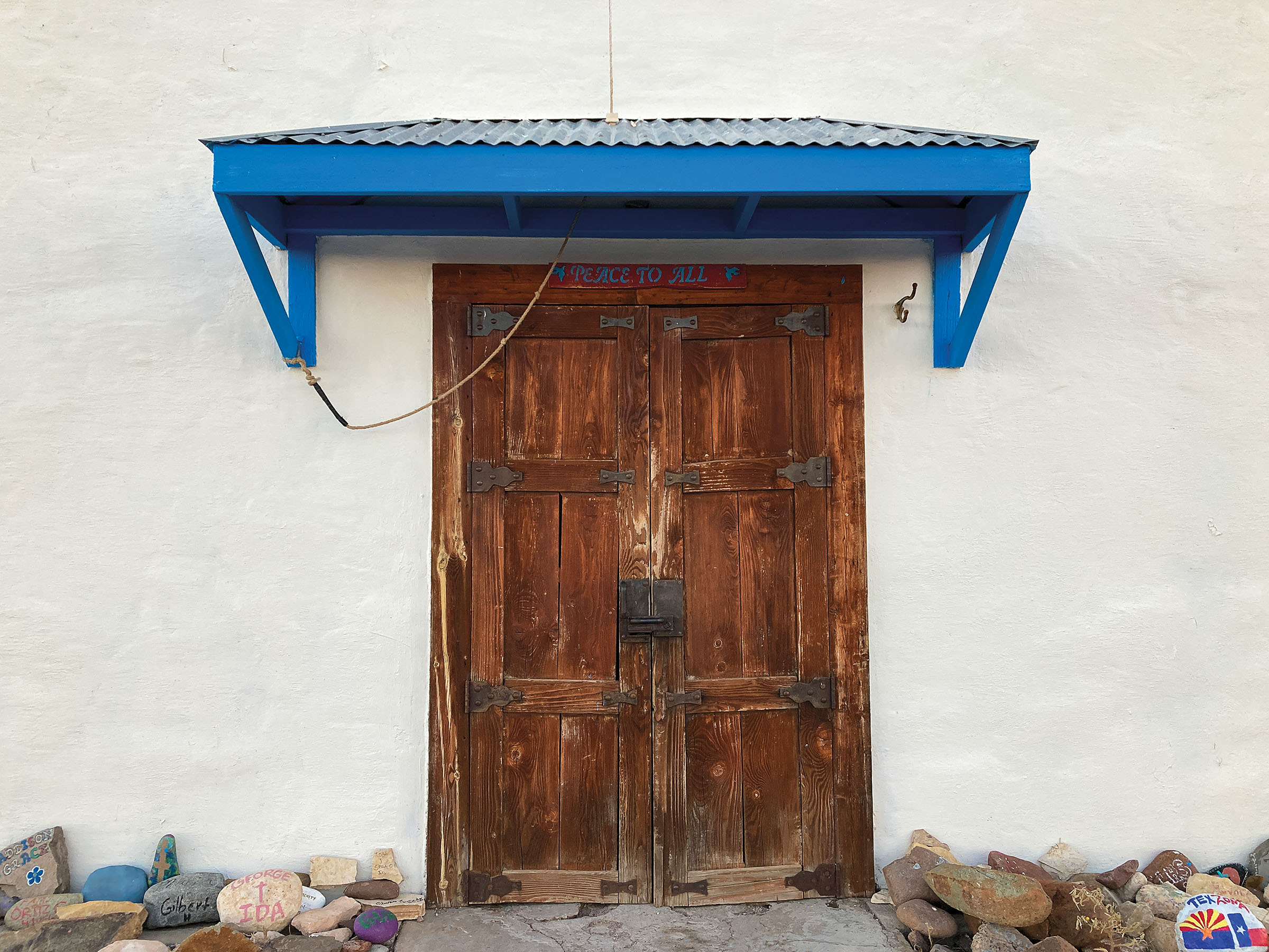 A bright blue awning adorns a rustic wooden door with metal hinges