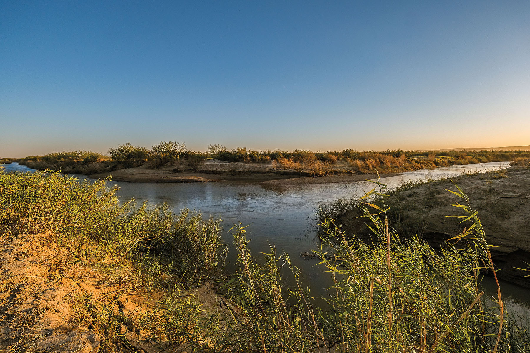 Two large flat rivers intersect under a blue and orange sunset sky