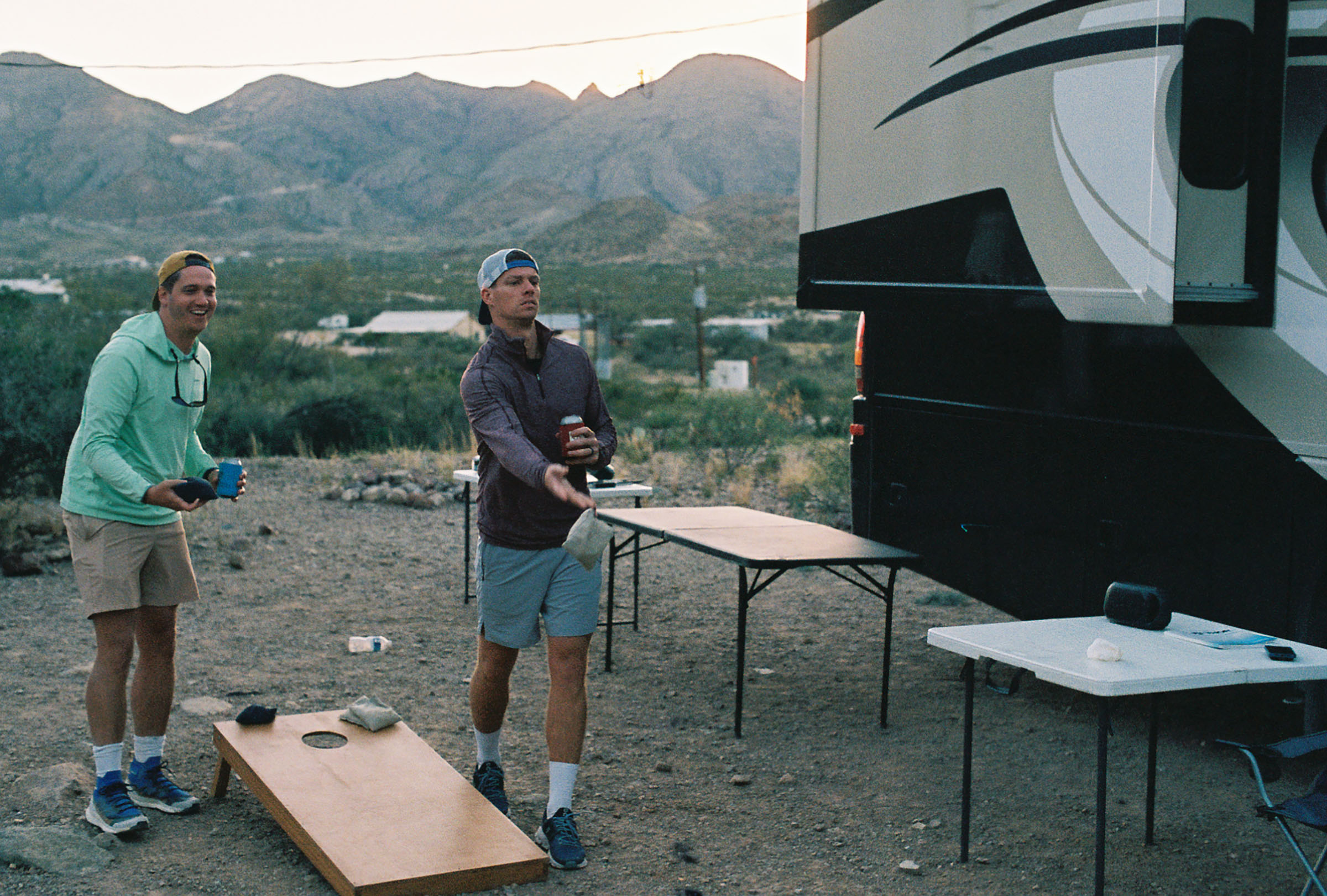 A pair of men play corn hole outside of an RV in the West Texas mountains