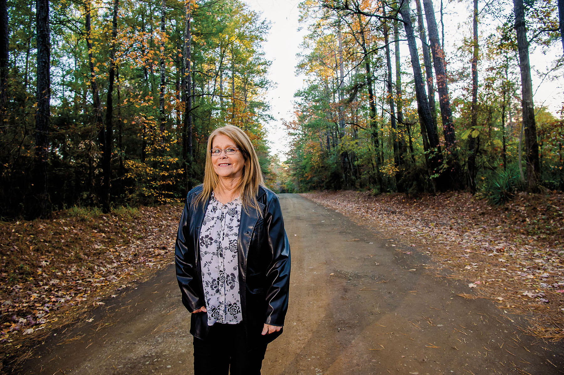 A woman stands on a road lined by tall trees