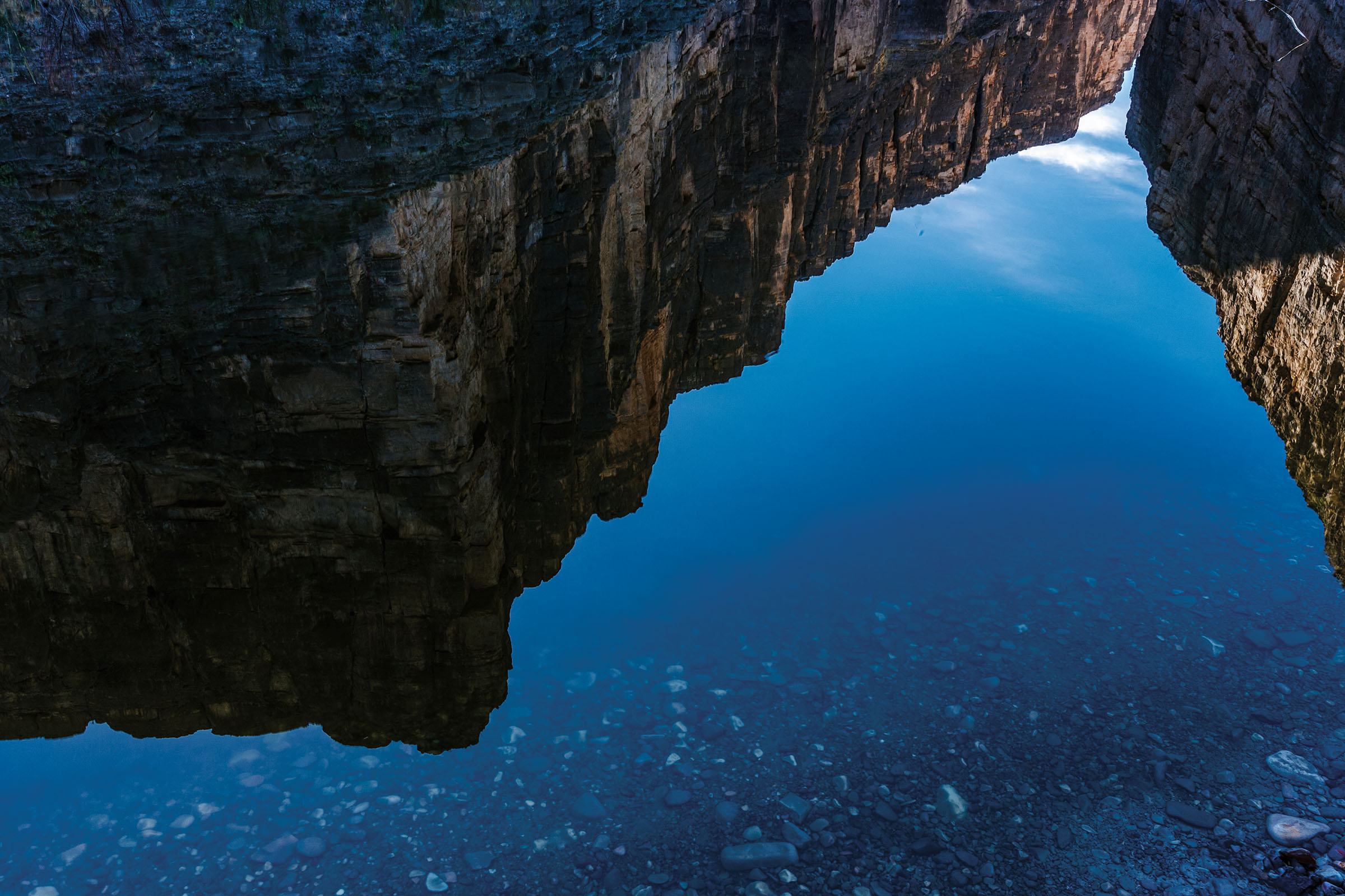 Tall rock canyons are reflected in blue water