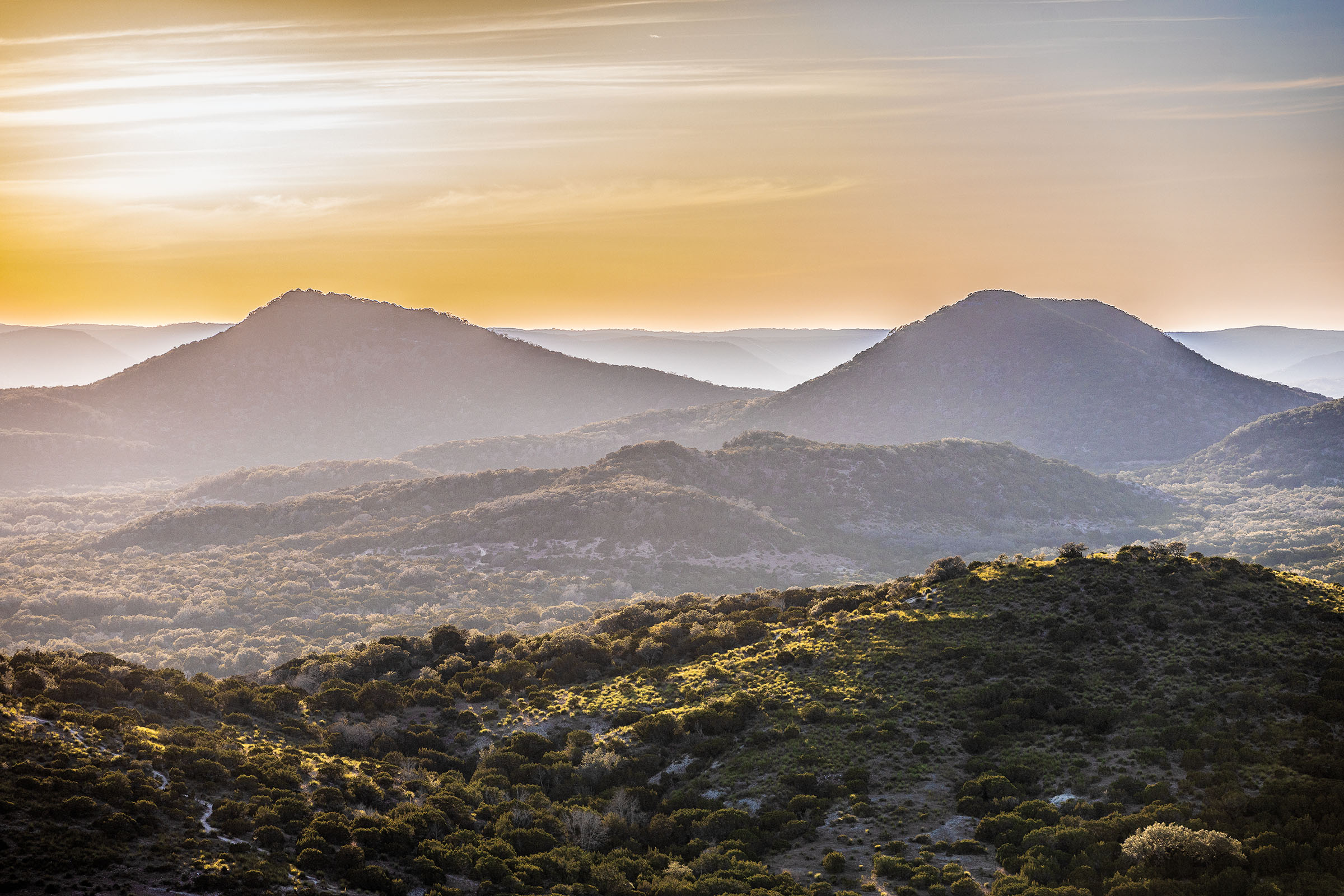 Short hills with rocks and shrubs dot the landscape of a hill country scene
