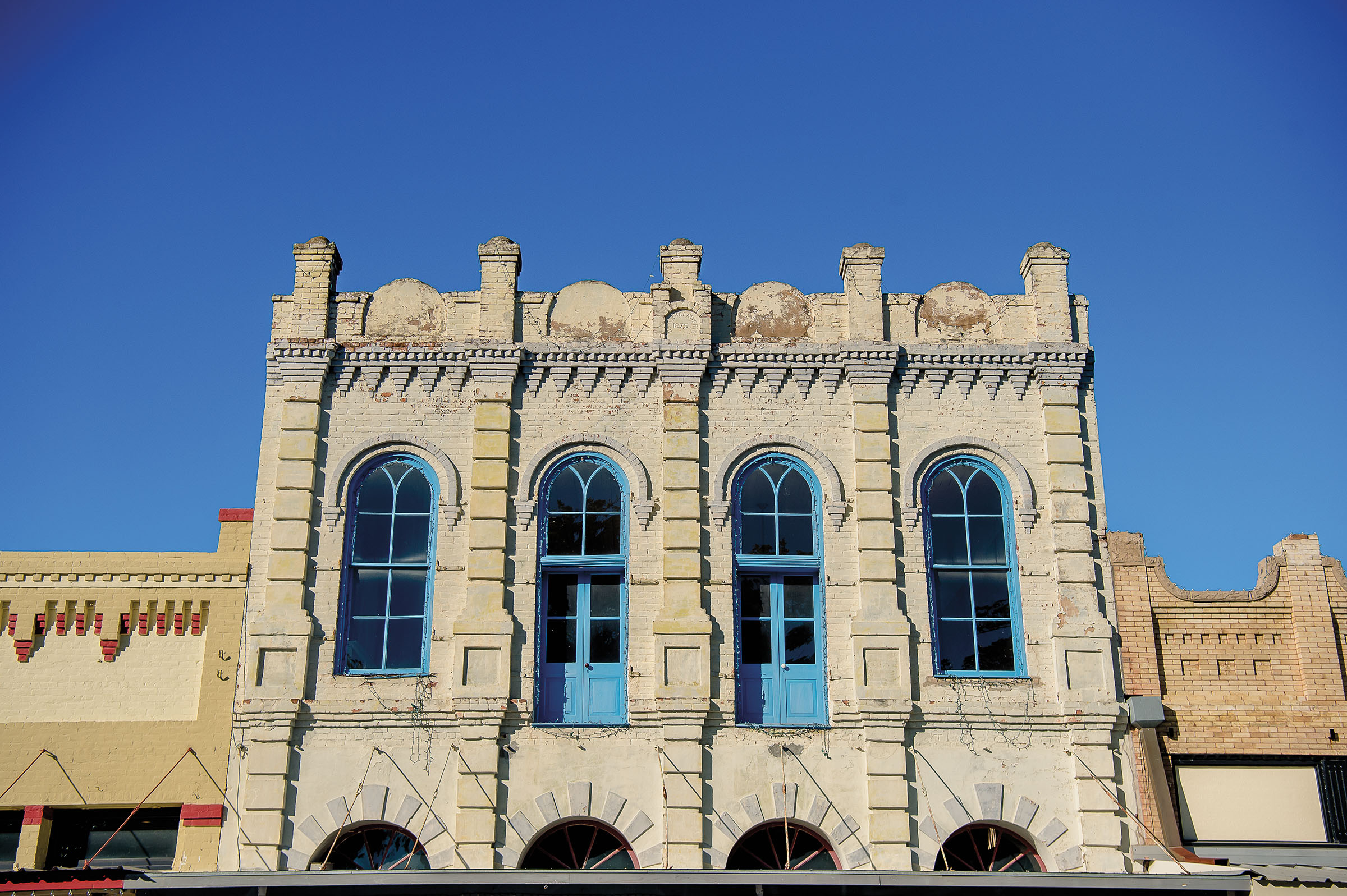 The exterior of a tan sone building with turquioise arches under blue sky