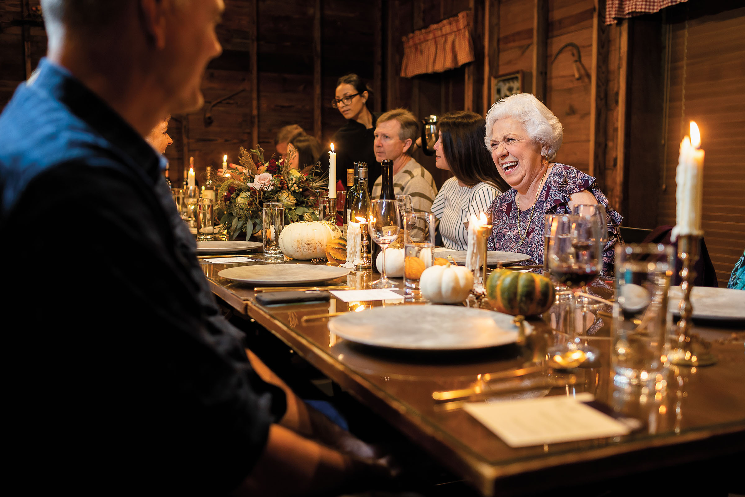 A small group of people sit around a richly decorated wooden table with candles