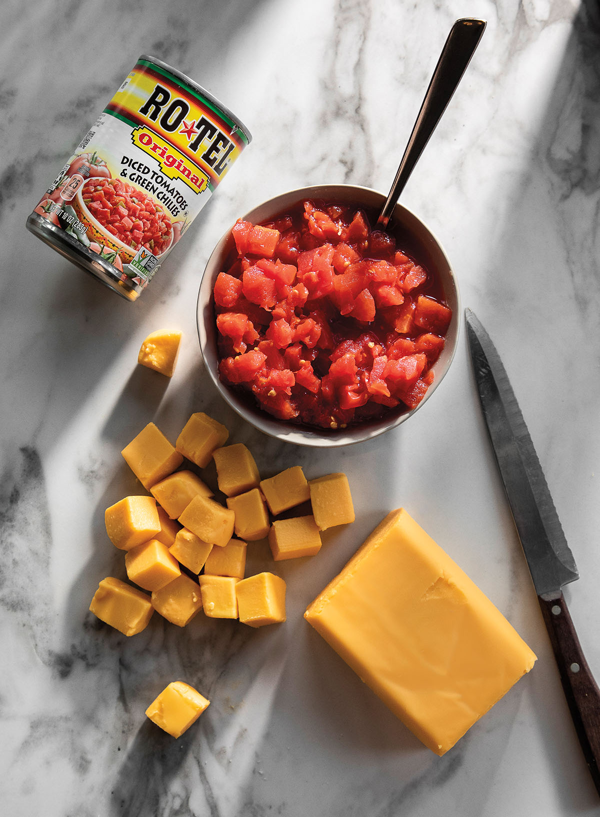 An overhead view of a can of Ro-Tel, the can emptied into a dish, and cubes of Velveeta cheese