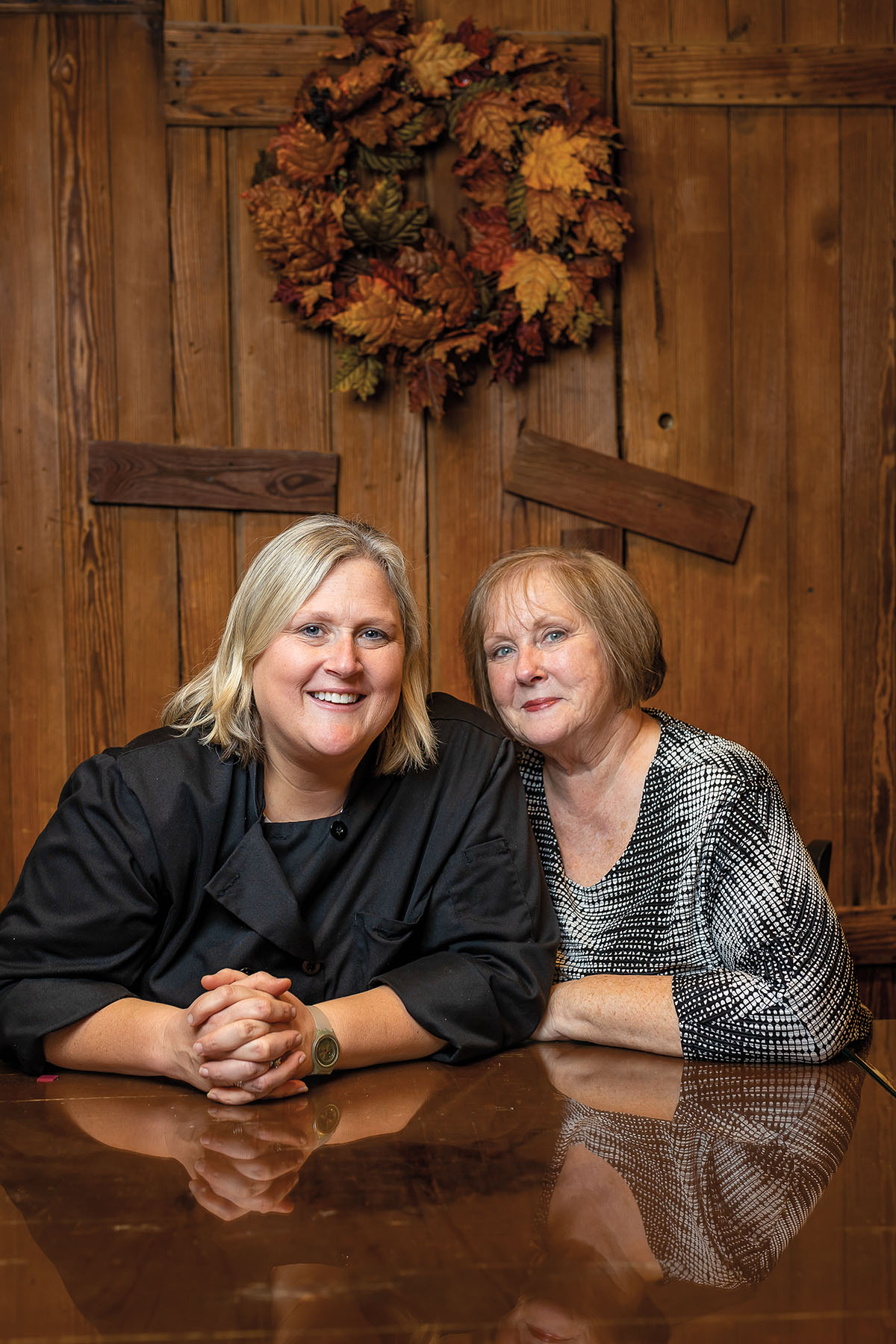 Two women sit in a wooden room at a glossy wood table