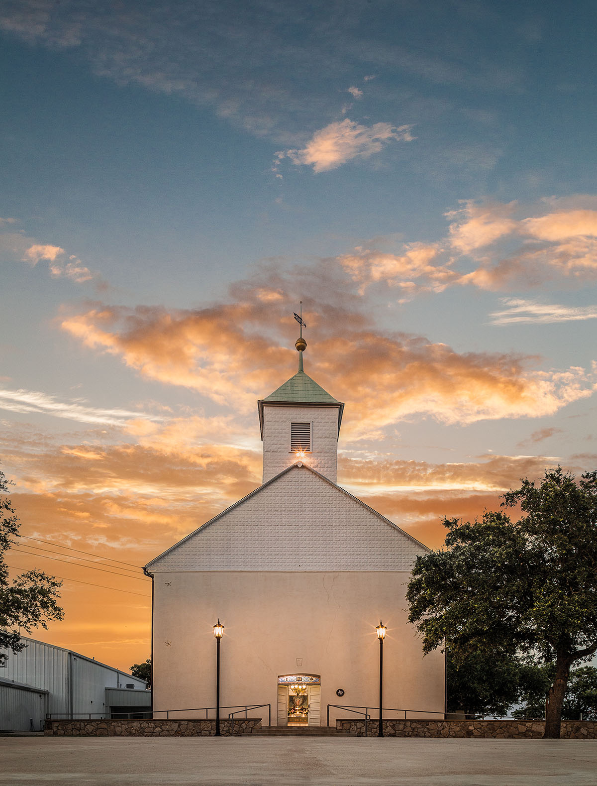 The exterior of a white chapel with a tall steeple in evening light with sparse clouds