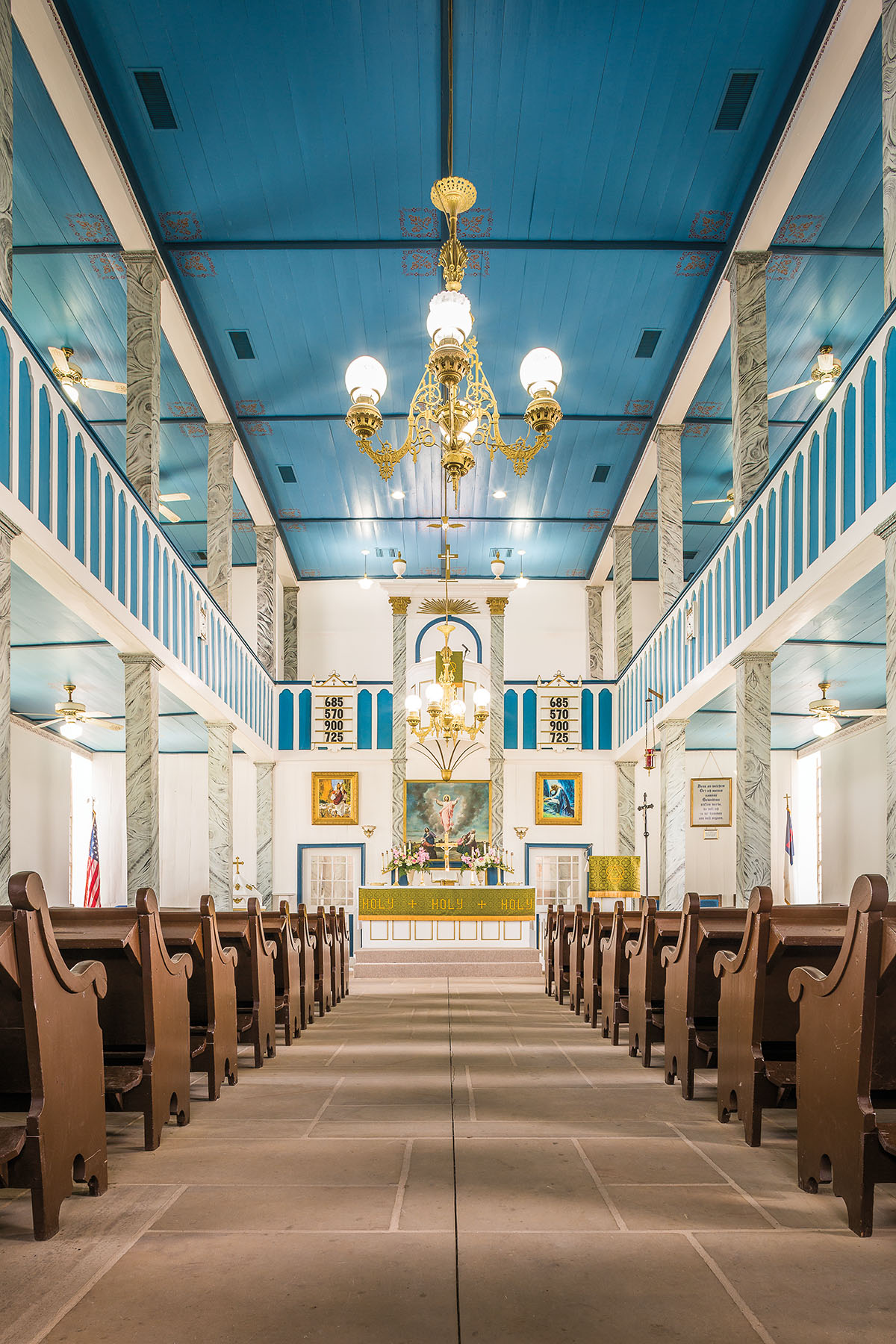 The inside of a church with dark brown pews and a brilliant blue ceiling with white accents and gold fixtures