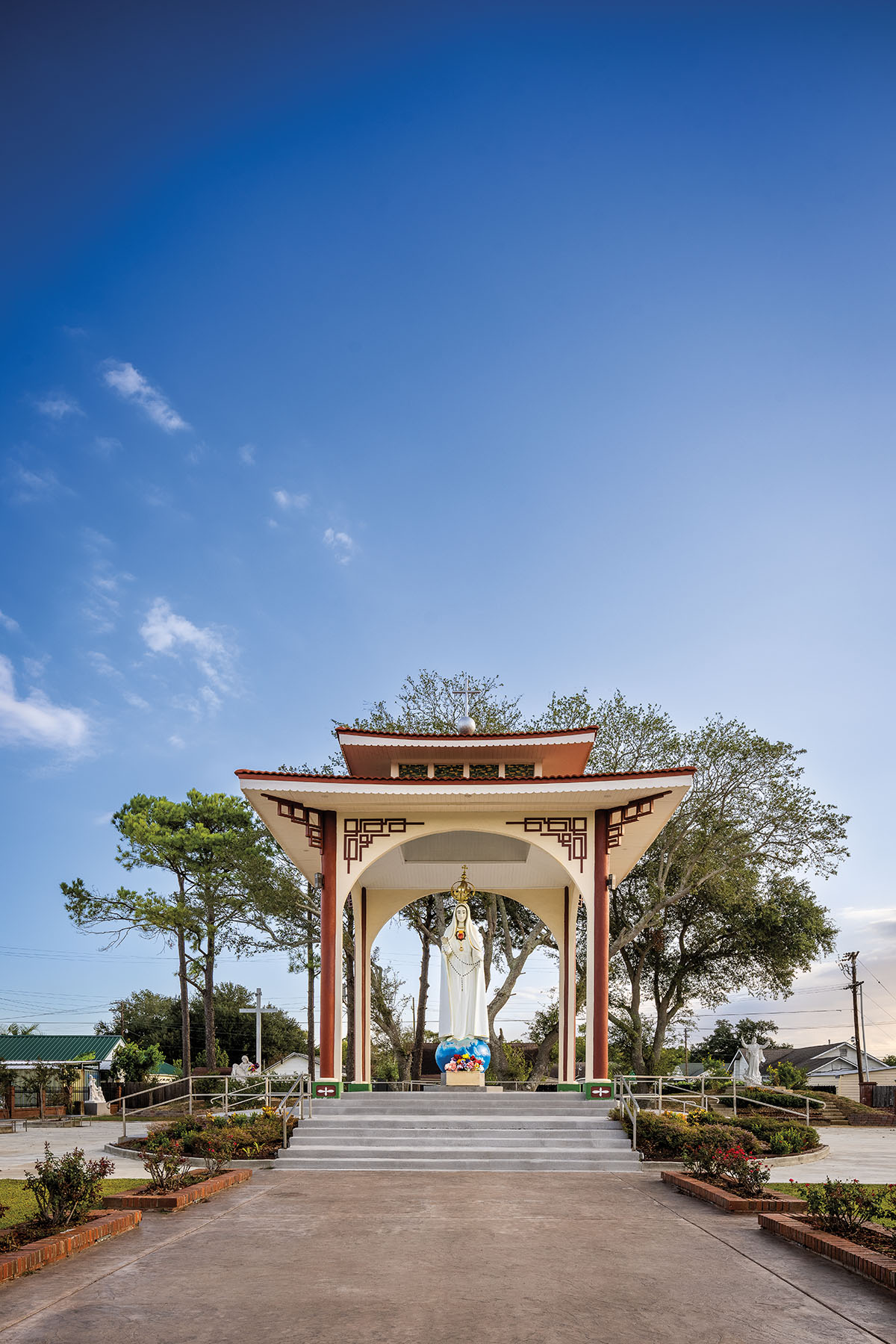 Curved, Vietnamese-style architecture in maroon and ivory adorn a sculpture of a female figure under a large blue sky