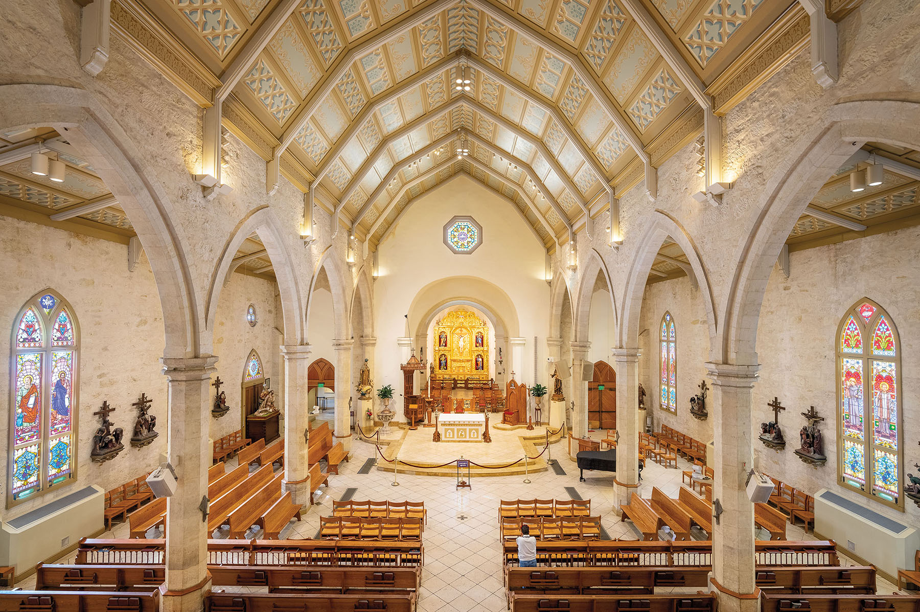 The interior of an ornate cream and gold chapel, with a few wooden chairs and pews under a vaulted ceiling