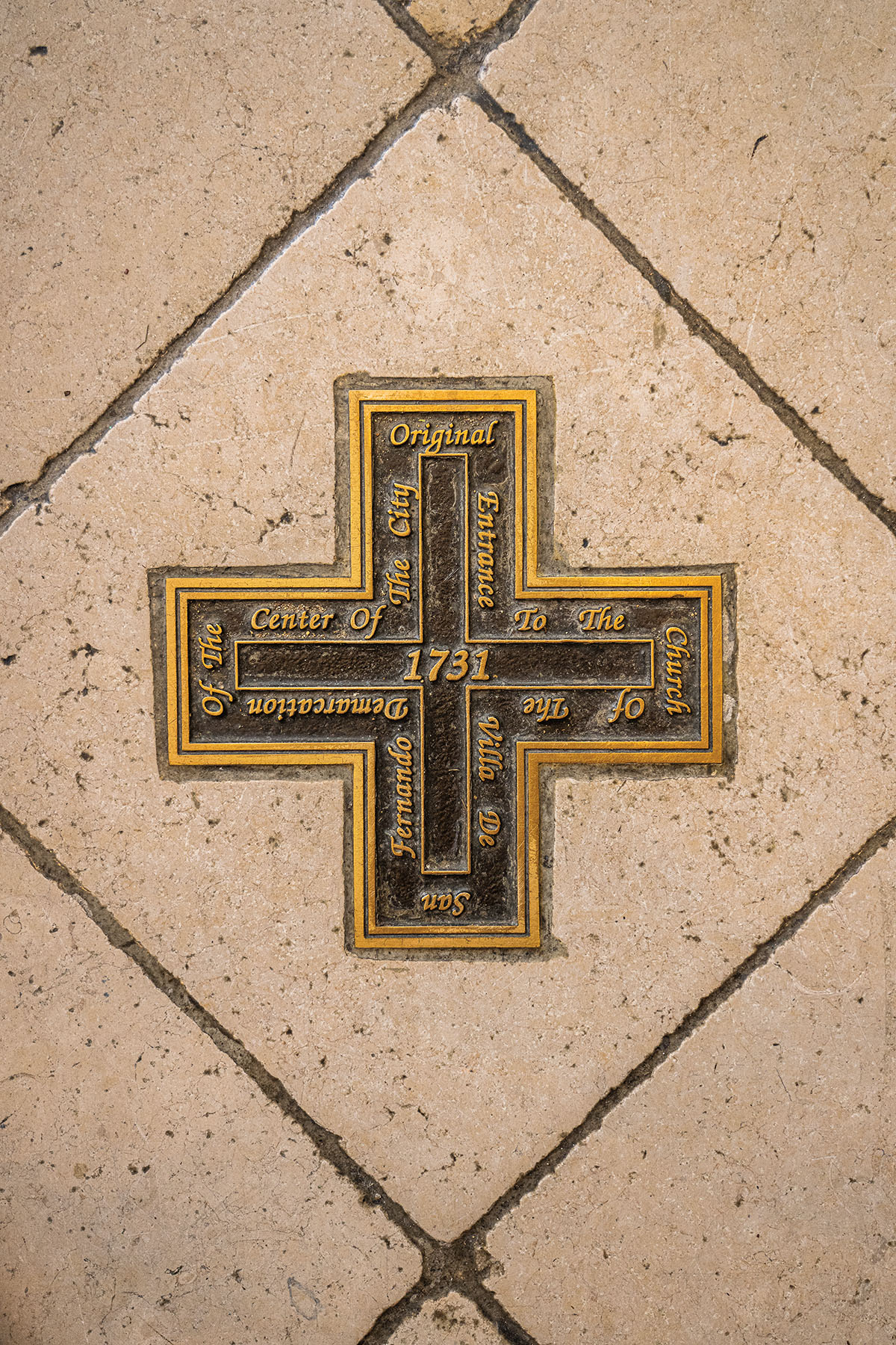 A dark cross inlaid in cream-colored tiel reading "Original entrance to the church"
