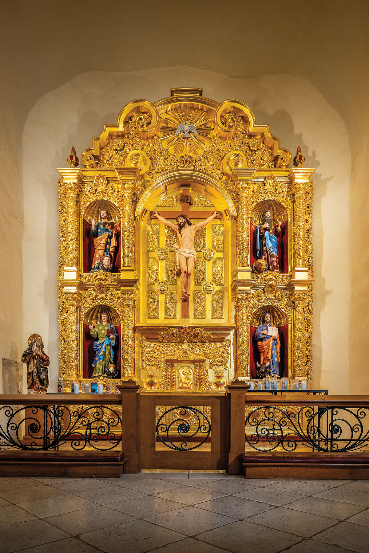 A golden shrine with Christ and other biblical figures behind a dark wooden railing