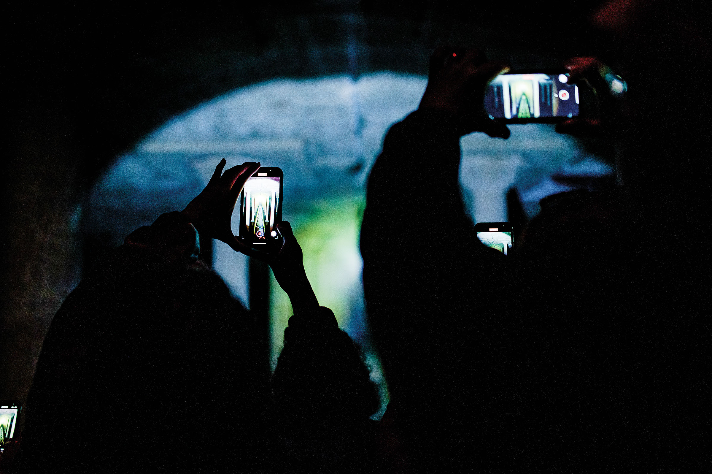 A group of people hold their phones up to take a picture in a dark environment