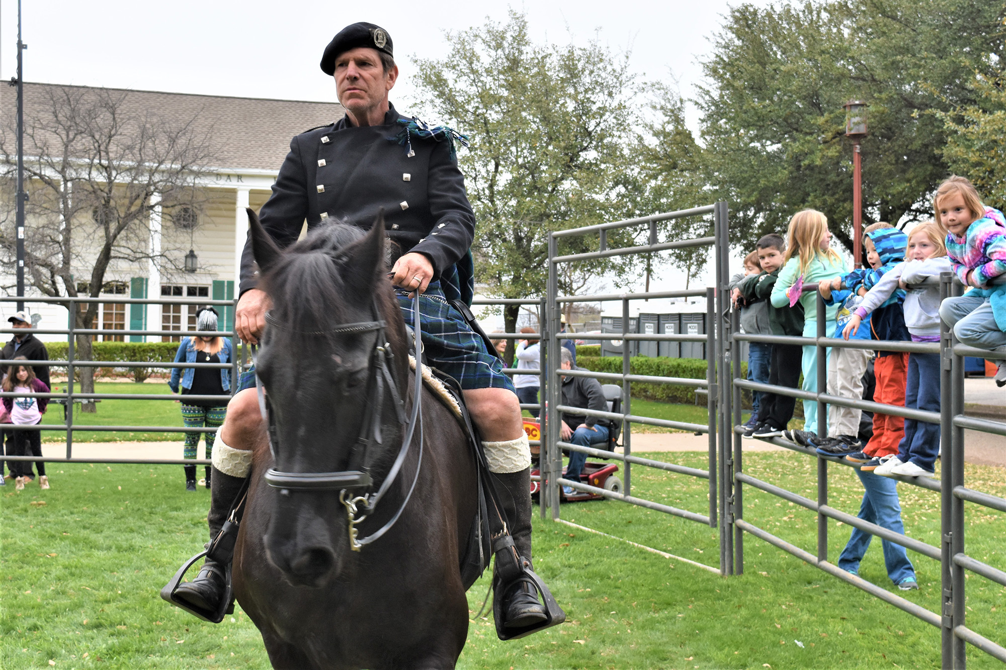 A man rides a horse for a small crowd. He is wearing traditional irish clothing with a buttoned jacket, hat, and kilt