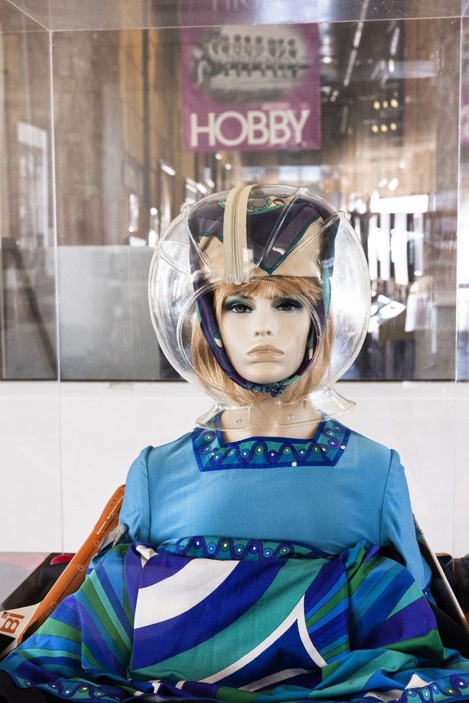 A mannequin wears a blue dress and clear plastic astronaut-type helmet.