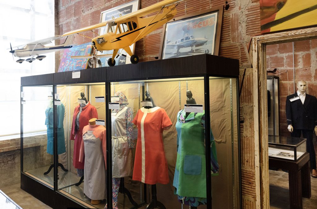A glass case holds a display with colorful flight attendant dresses.