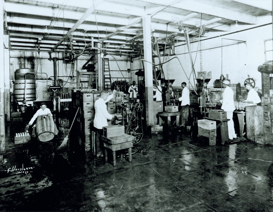 A black and white picture of a group of people in white shirts working with large metal equipment in a factory setting