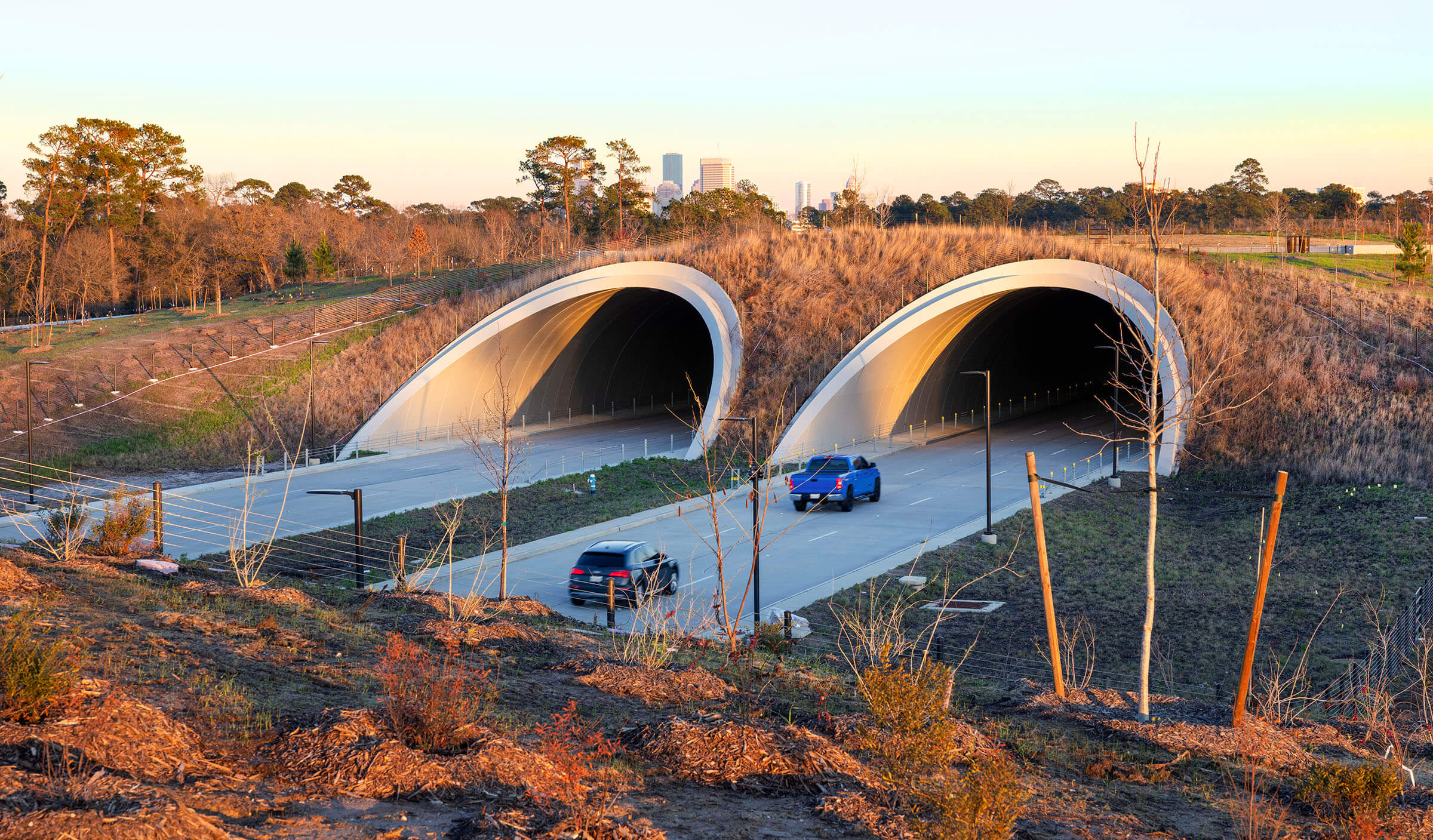 Vehicles drive on a concrete roadway into large concrete tunnels built into a tract of land