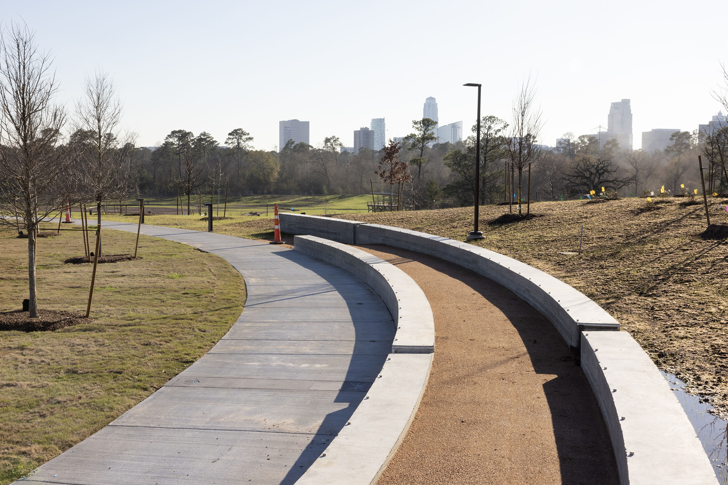 A gray concrete sidewalk next to a grassy area with downtown Houston in the background