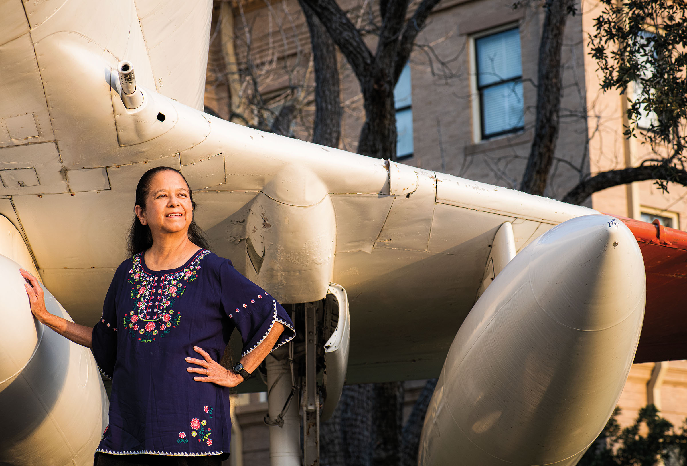 A woman in a purple shirt stands in front of a replica of an airplane in front of a stone courthouse