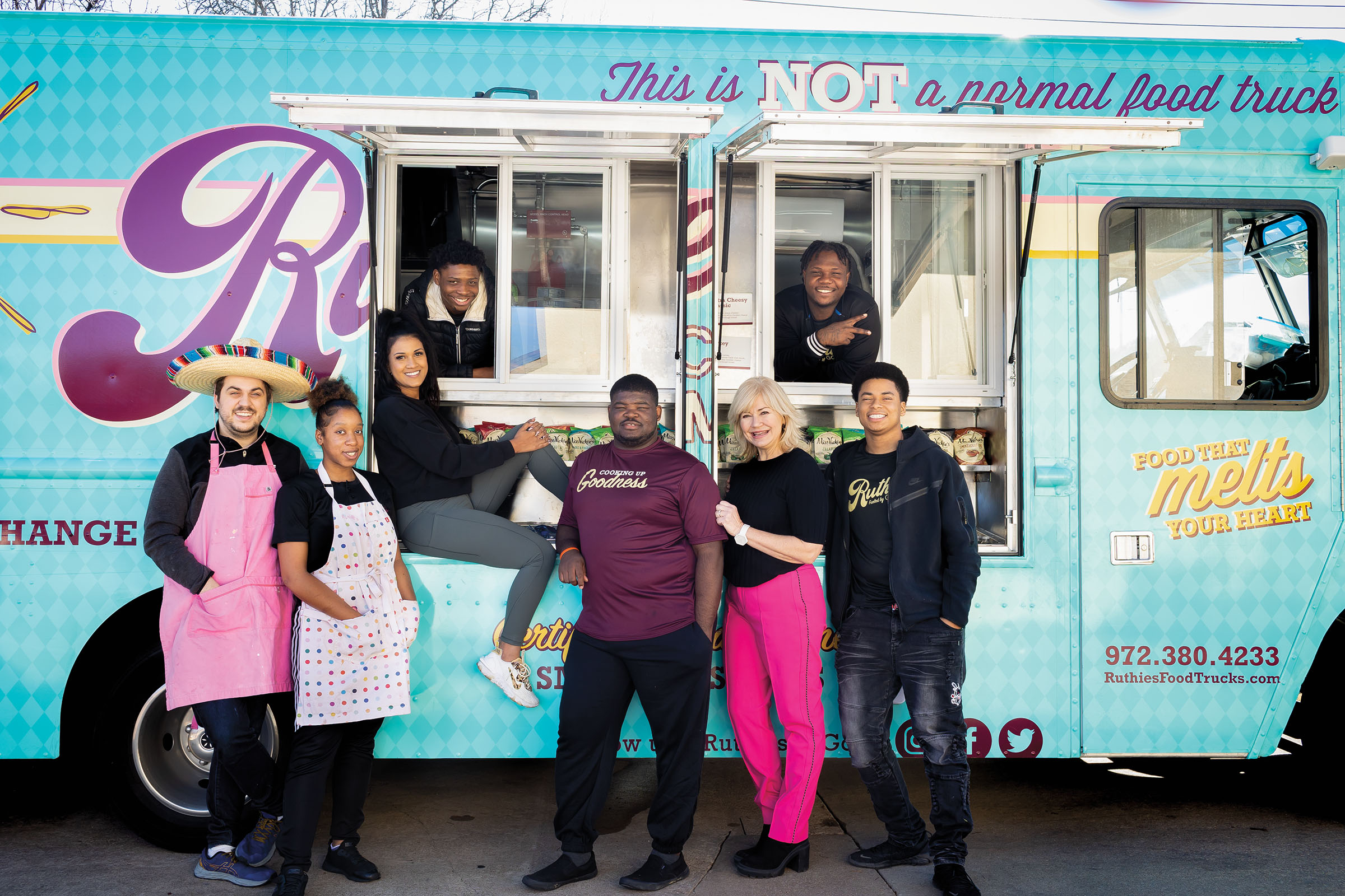A group of people stand outside of a turquoise food truck