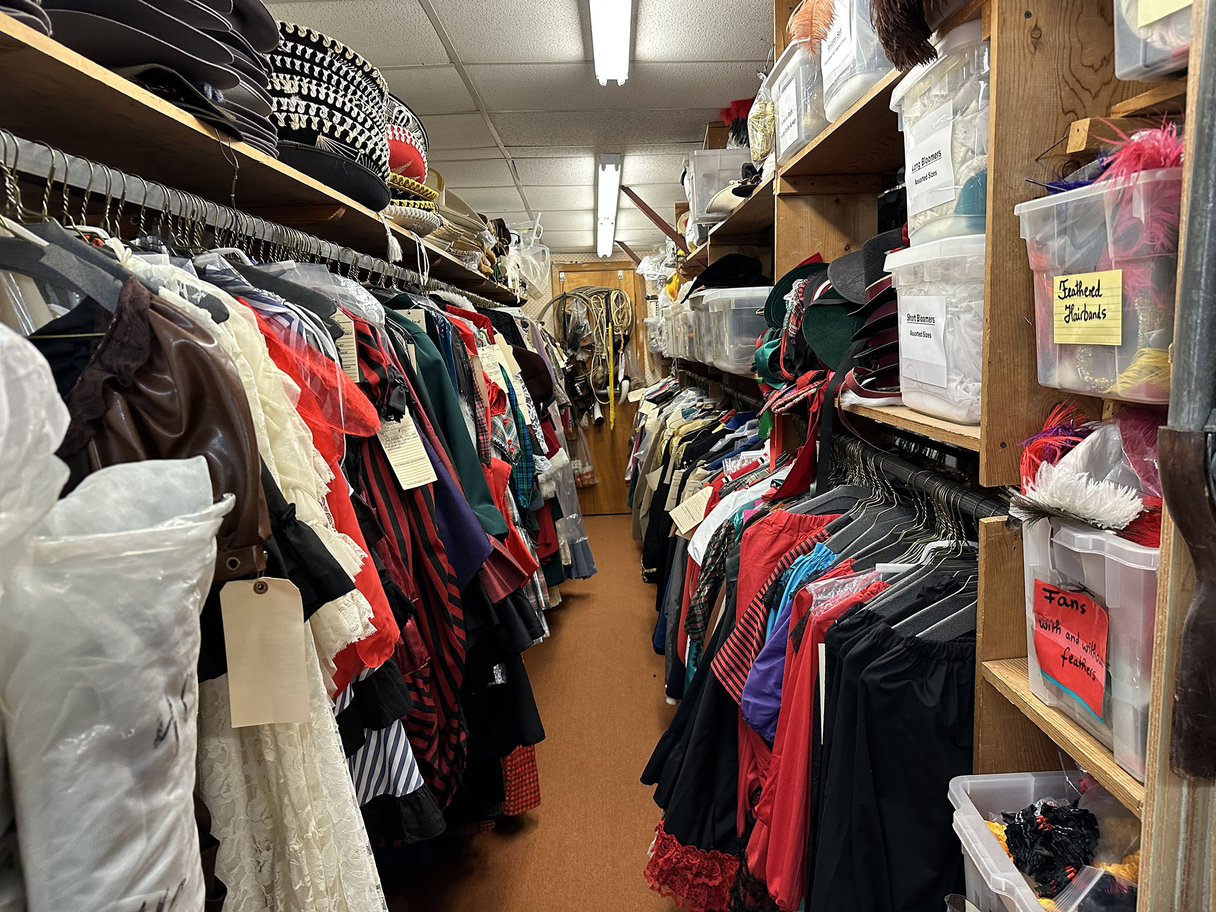 Costumes and other items line two walls of a narrow aisle inside the shop. 