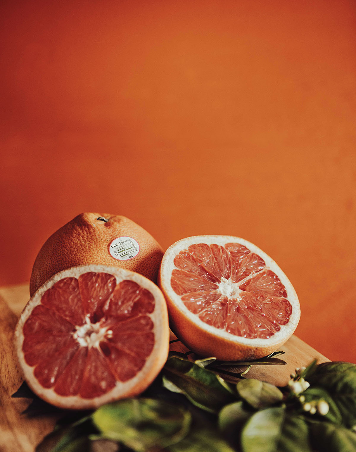 A bright red grapefruit split in half on a wooden cutting board in front of an orange wall