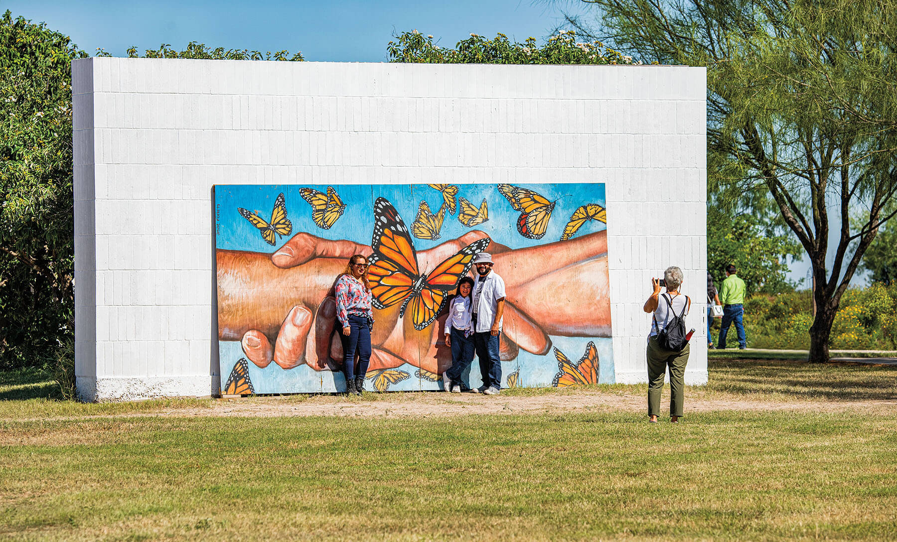 A group of people take pictures in front of a large butterfly mural