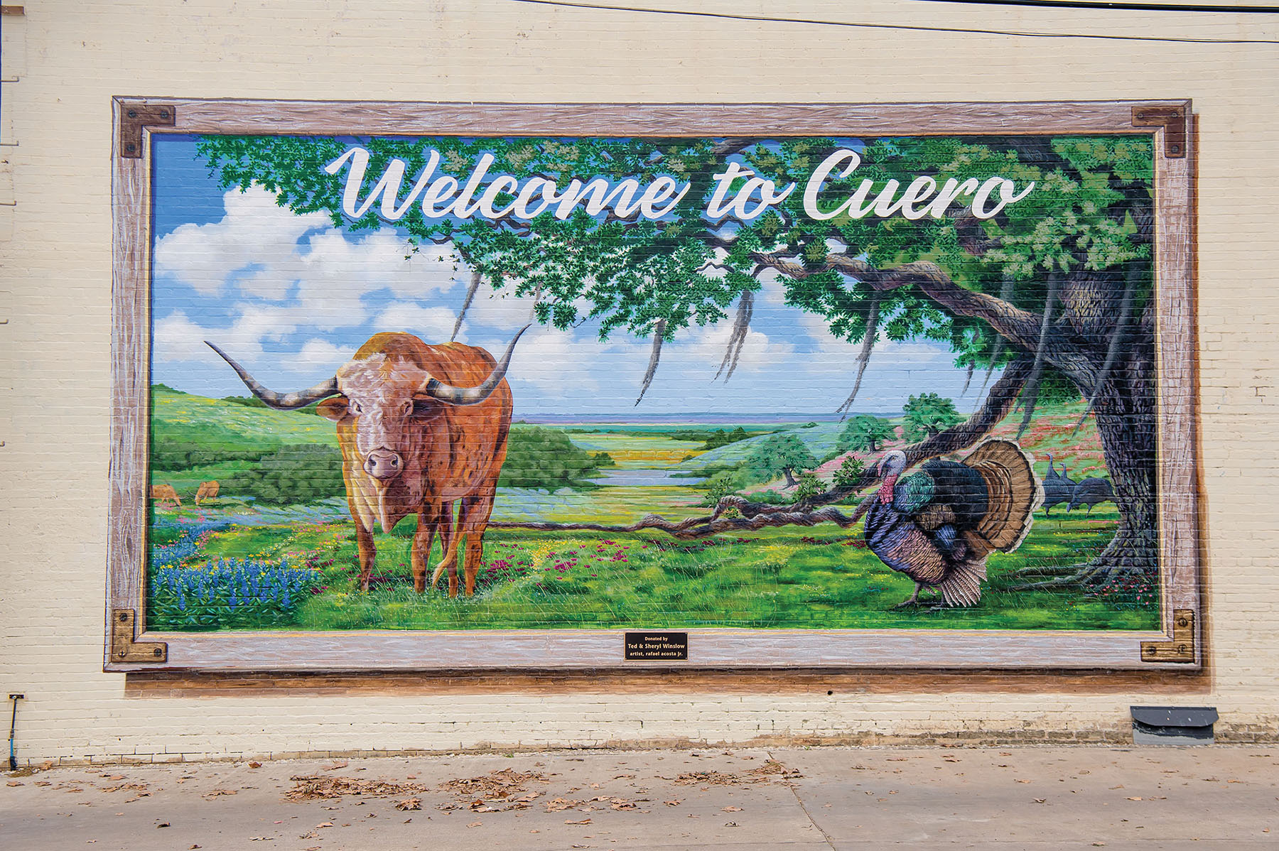 A mural of a cow and turkey in a natural scene with type reading "Welcome to Cuero"