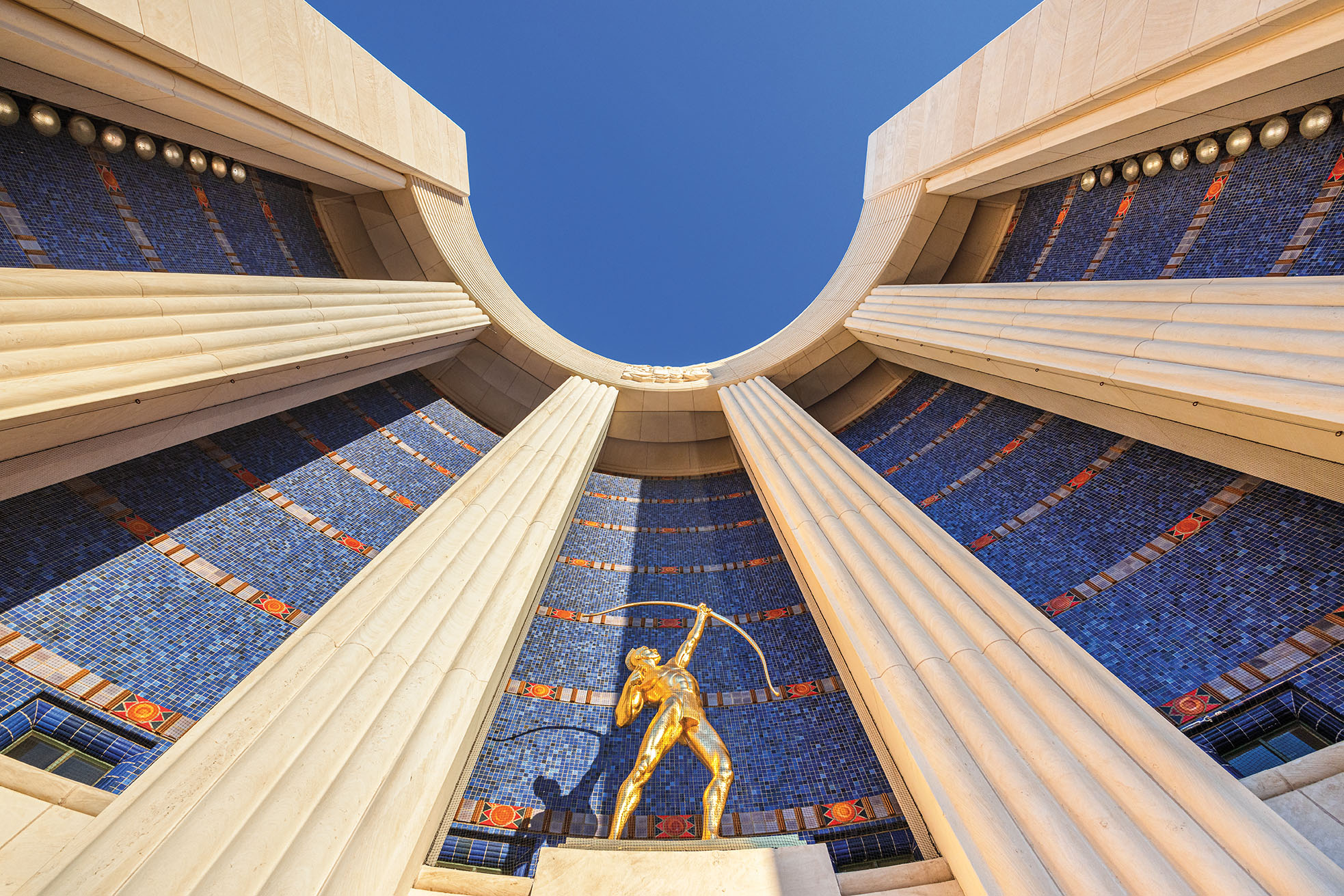 View looking upward at Allie Victoria Tennant's "Tejas Warrior" statue and the curved exedra (semicircular architectural recess) at the front entrance of the Hall of State building at Fair Park in Dallas.