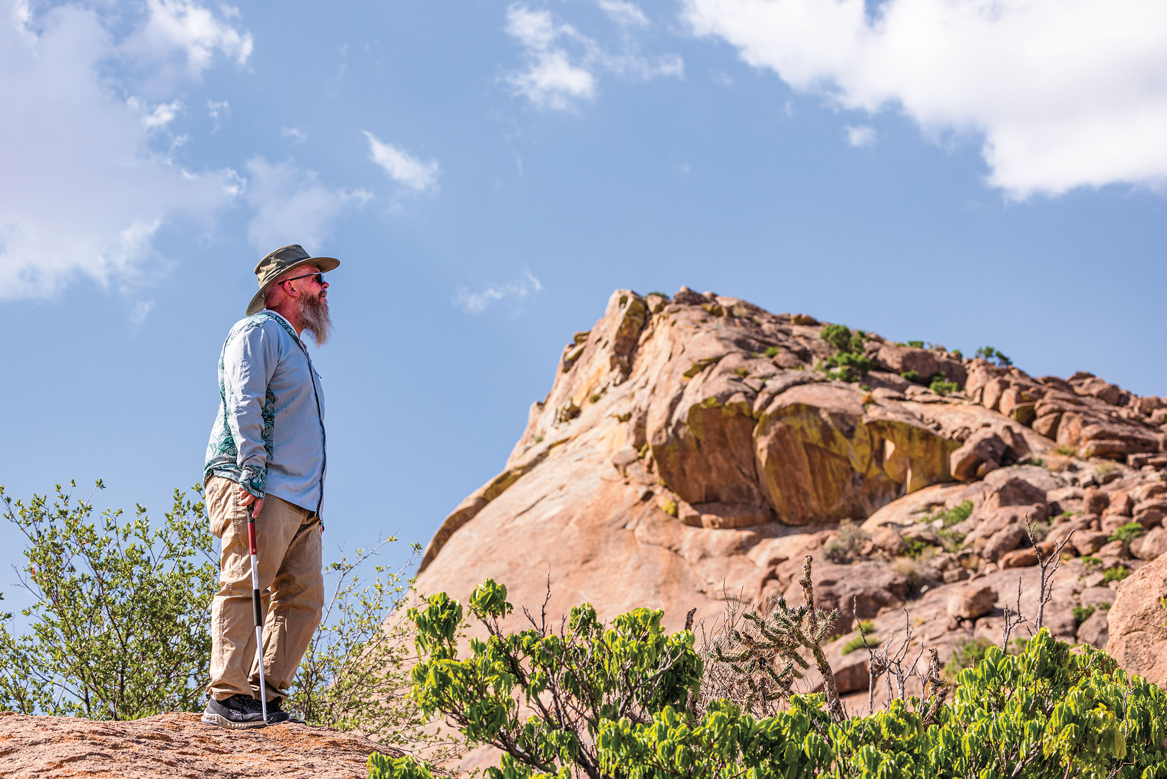 A man in outdoor gear and a hat looks up at a rock formation