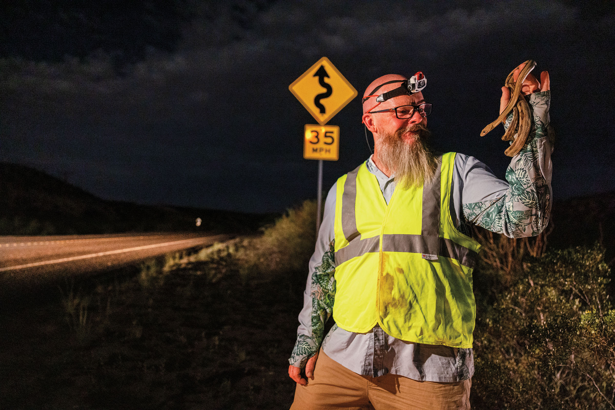 A man in a high-visibility green vest holds a snake