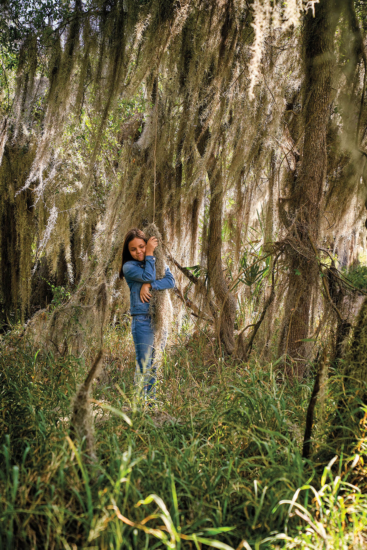 A young woman in a blue shirt hugs a large piece of moss in the woods