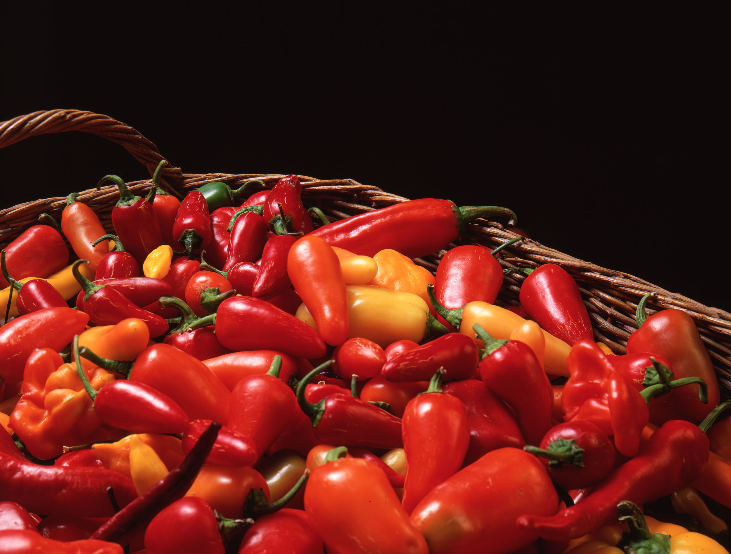 A basket of bright red, orange, and yellow peppers on a black background