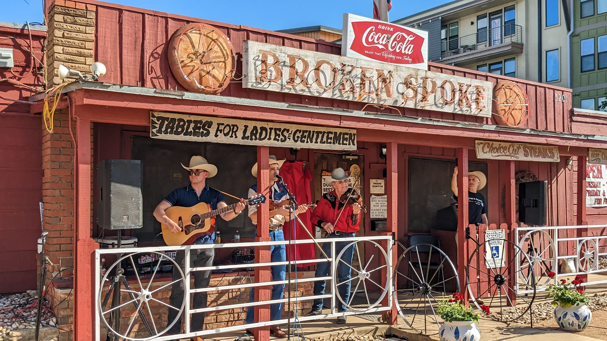 On the narrow patio of honky-tonk Broken Spoke, musicians Alvin Crow and Ian Stewart, dress in western attire, perform with acoustic guitars.