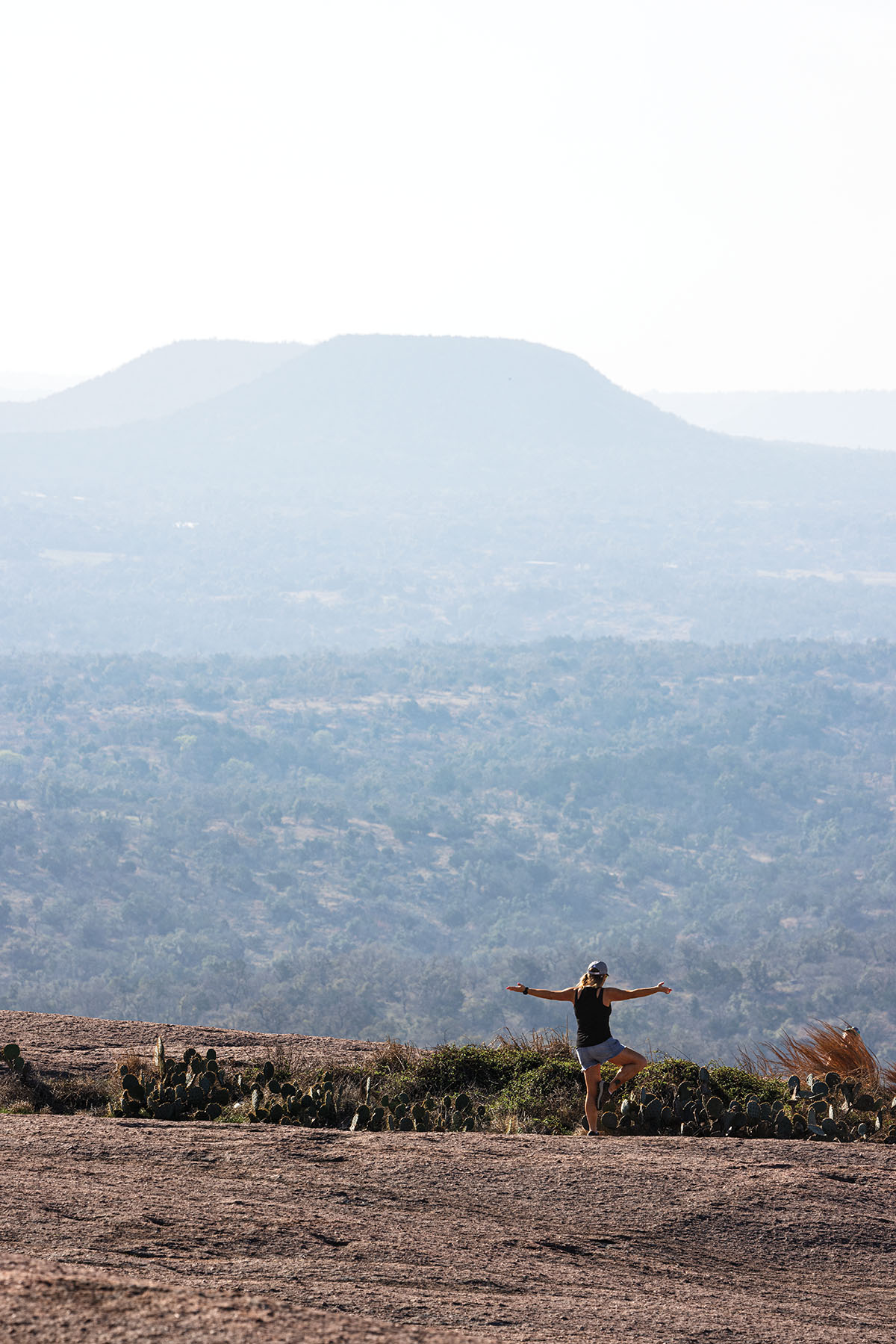 A person stands on Enchanted Rock in a yoga pose with a large formation in the background