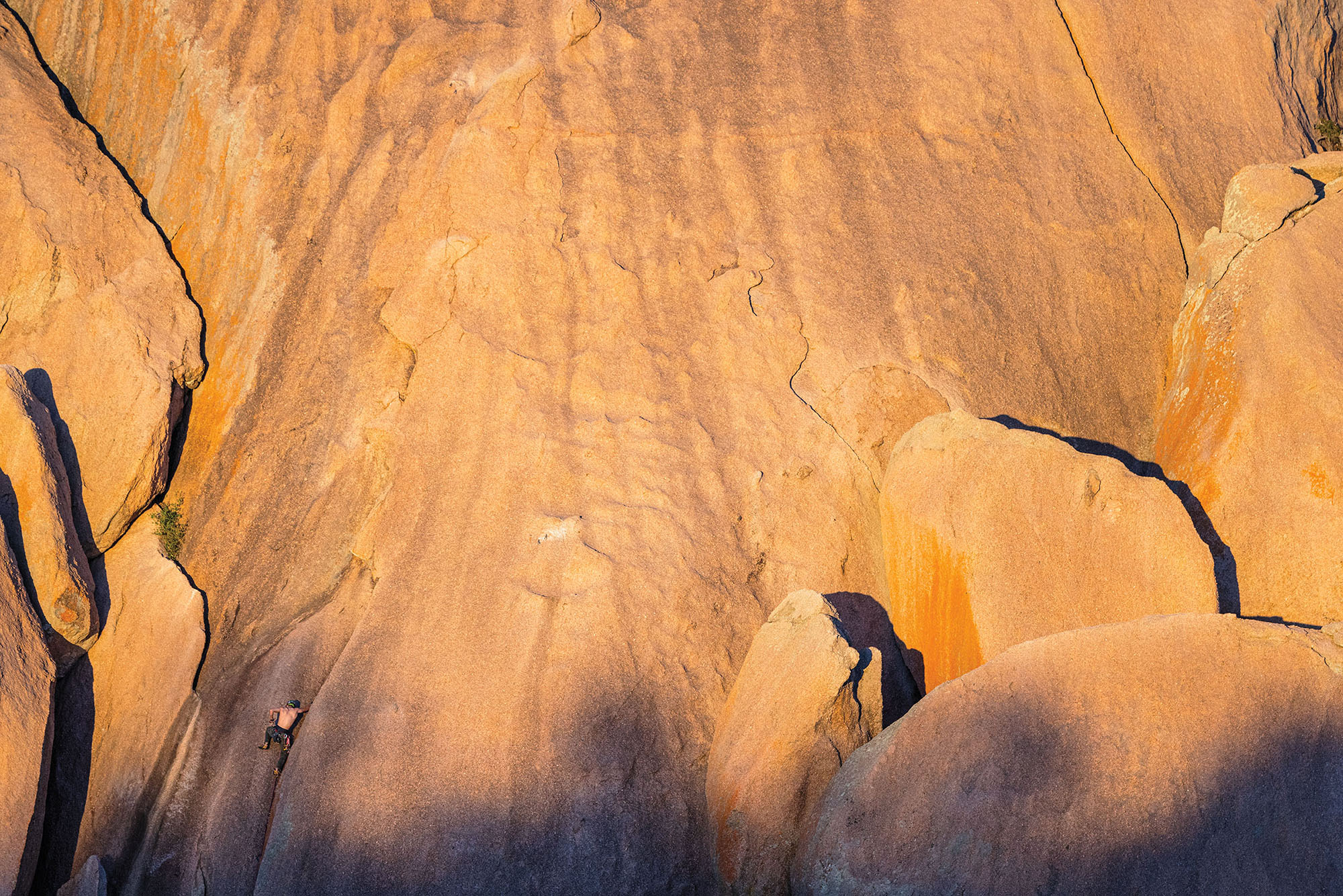A climber makes their way up a sheer rock face with a few shadows bathed in golden afternoon light