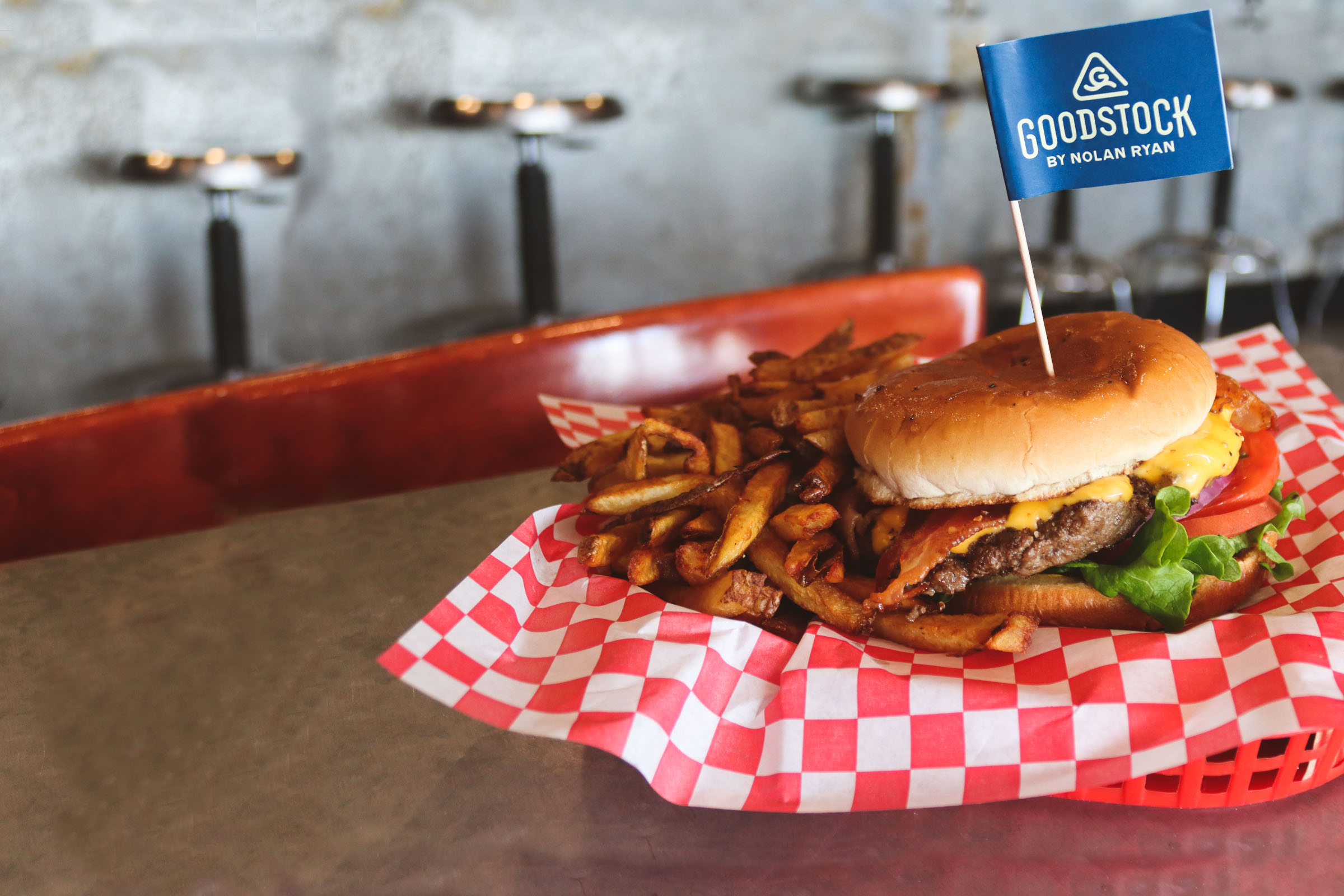 A burger and fries served in a red-checkered basket with a small blue flag toothpick reading "Goodstock"