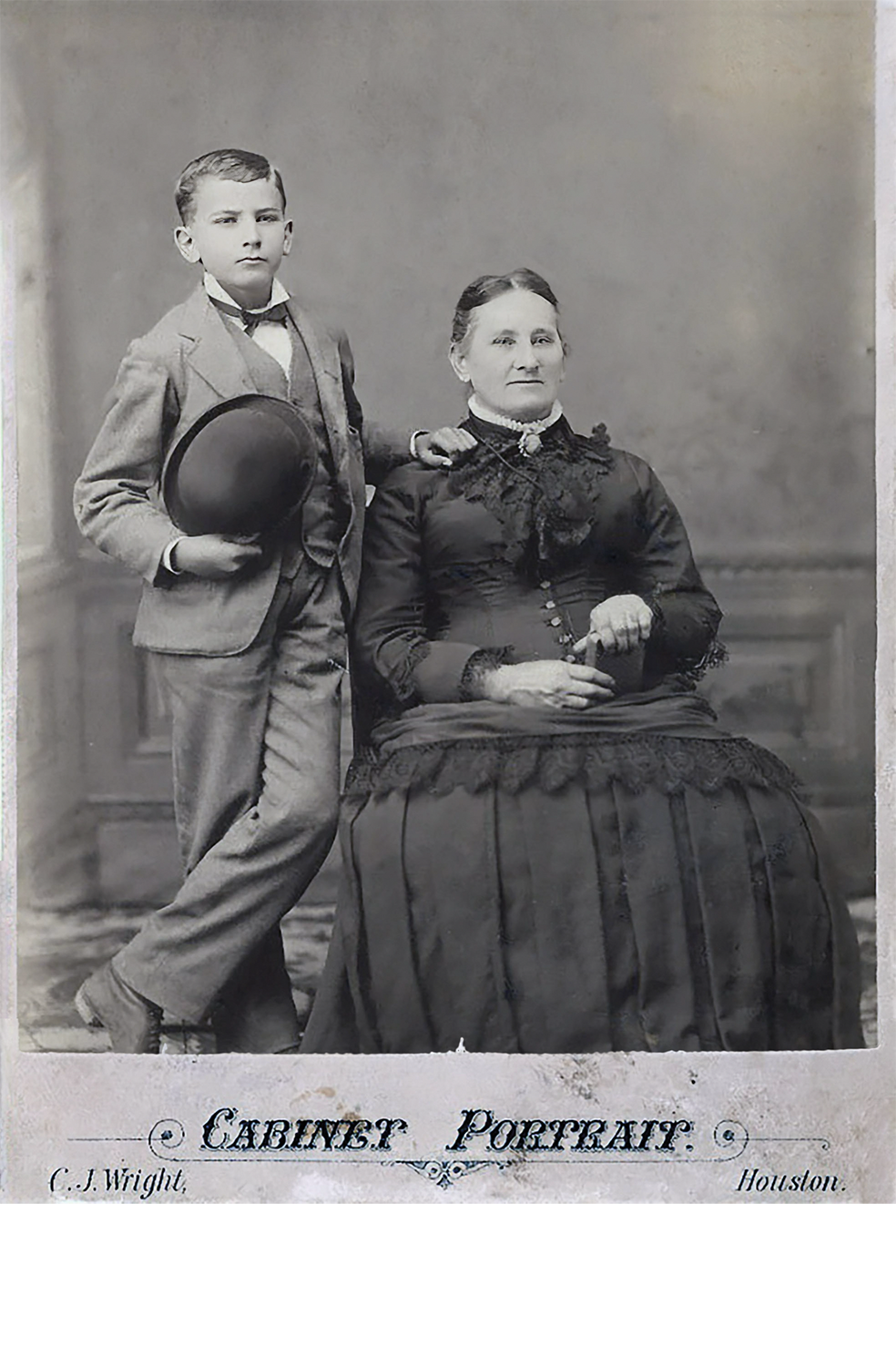 A boy stands next to his mother who is seated for a portrait circa 1880.